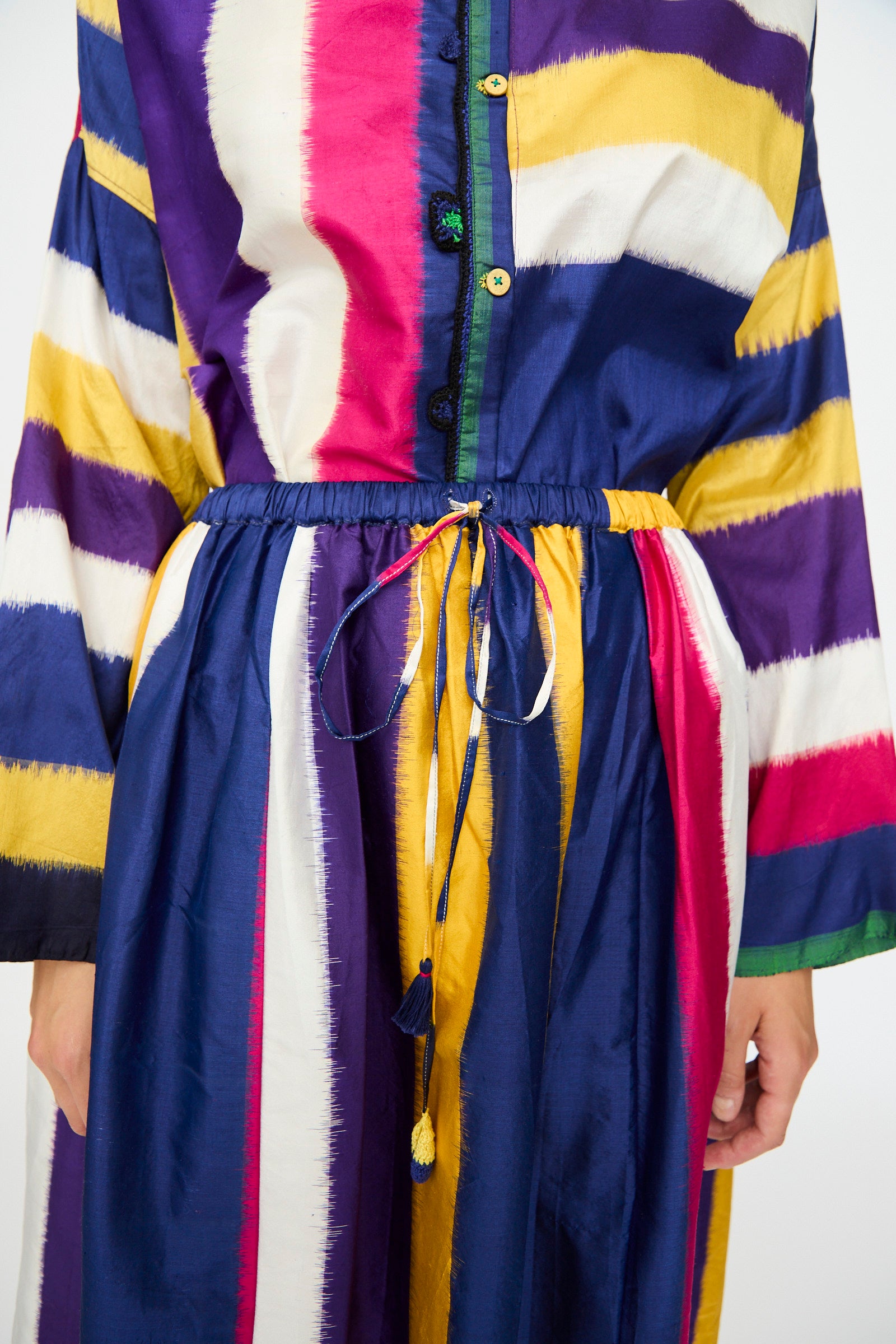 A person wearing the Injiri Ikat Silk Skirt lined with Cotton, featuring multi-color stripes in blue, yellow, red, white, and purple.