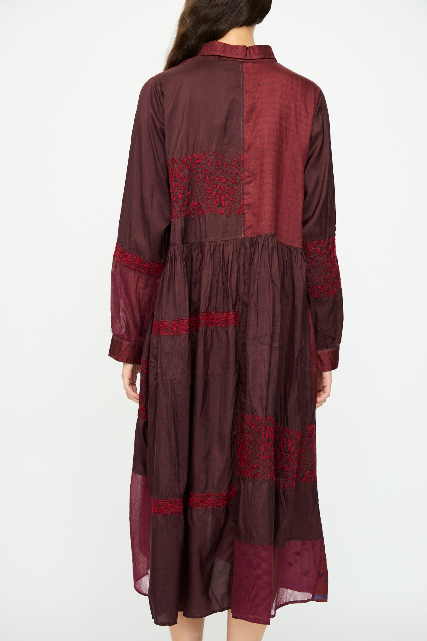A woman is seen from the back wearing the Injiri Silk and Cotton Dress in Red, featuring long sleeves, red lace accents, and a subtle geometric pattern, photographed against a plain white background.