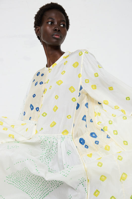 A woman in a Silk Dress in White adorned with yellow and blue geometric patterns by Injiri, posing against a white background.