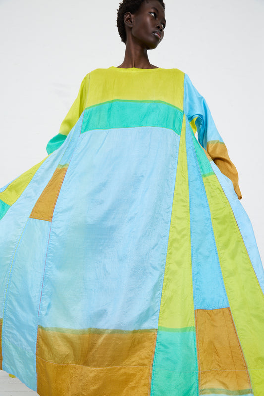 A model wearing a brightly colored patchwork Injiri silk dress in yellow and blue panels, standing against a white background.