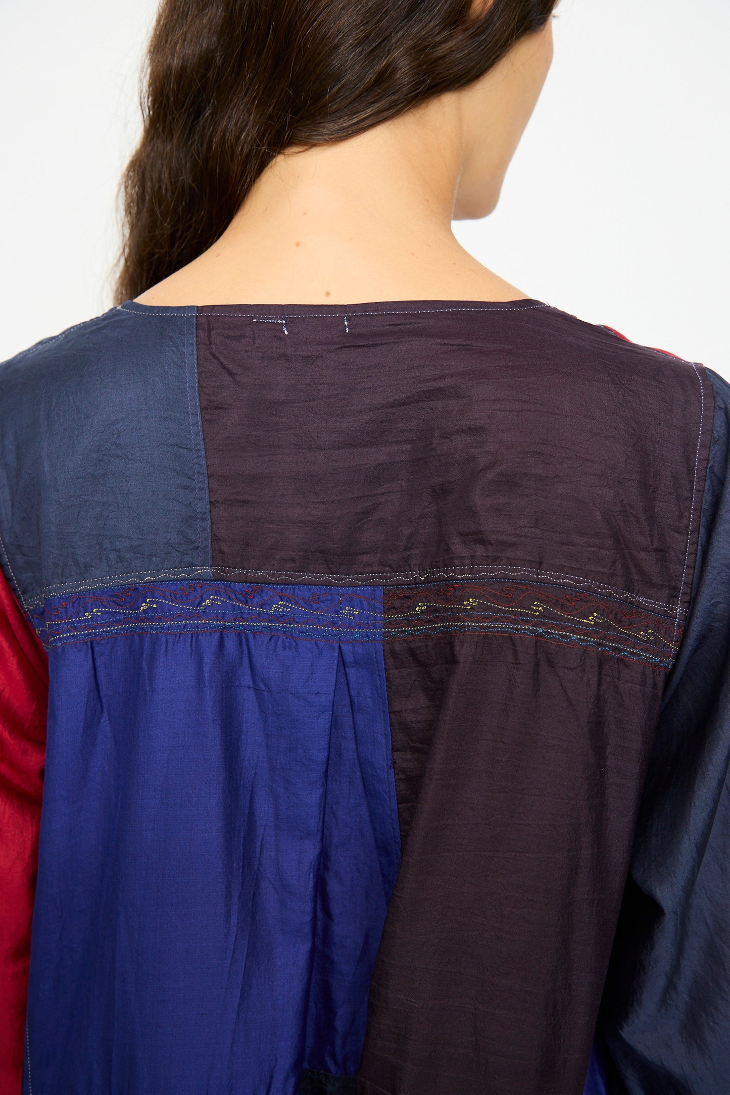 A person with long brown hair is shown from behind, wearing the Injiri Silk Dress in Red, Blue and Yellow Multi. The relaxed-fit dress features color-blocked panels and subtle stitching detail.