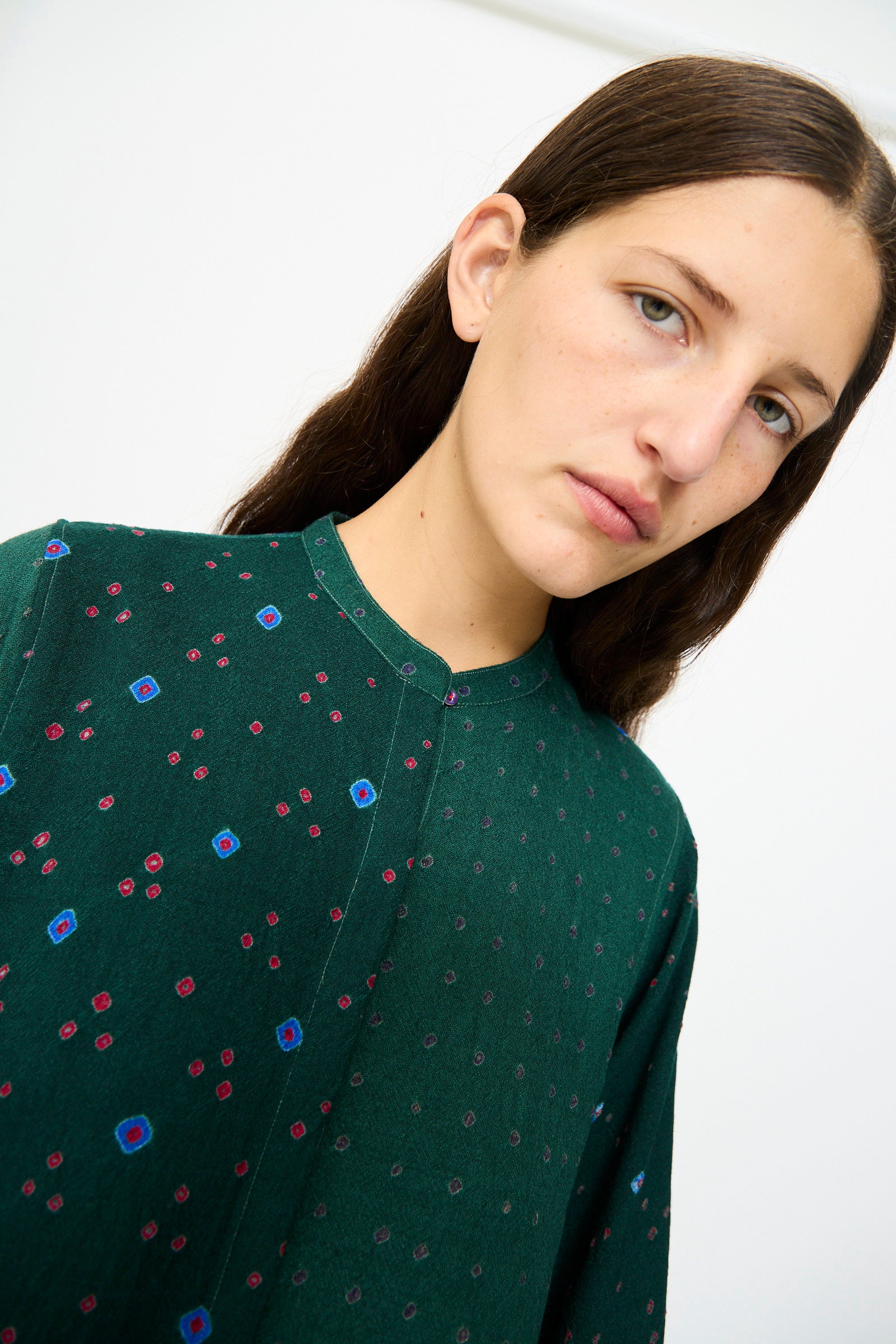 A person with long brown hair wears the Injiri Wool Dress in Green, featuring a geometric patchwork design, standing against a plain white background.