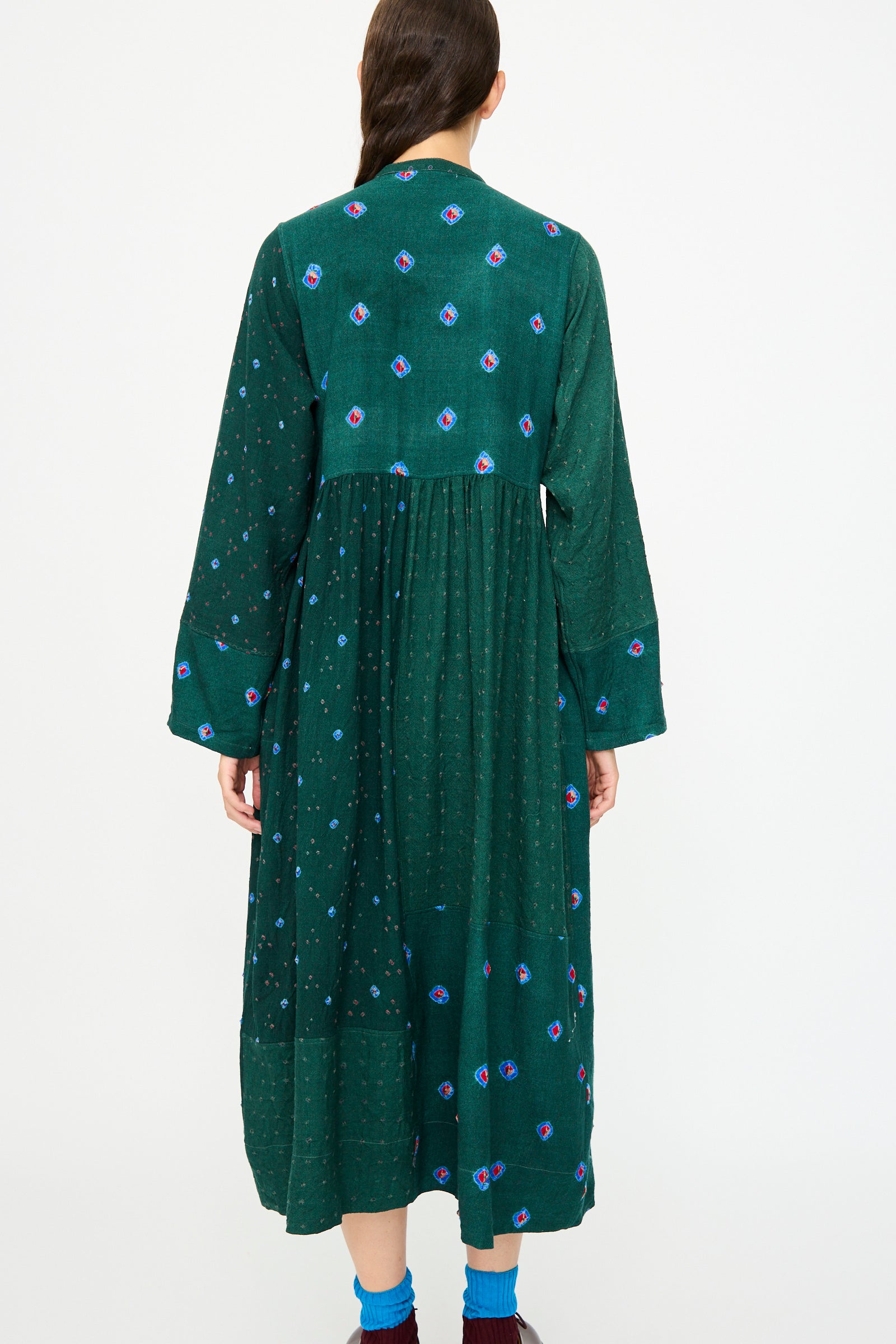 A person is seen from behind wearing the Injiri Wool Dress in Green, featuring long sleeves and small blue and pink patterns.