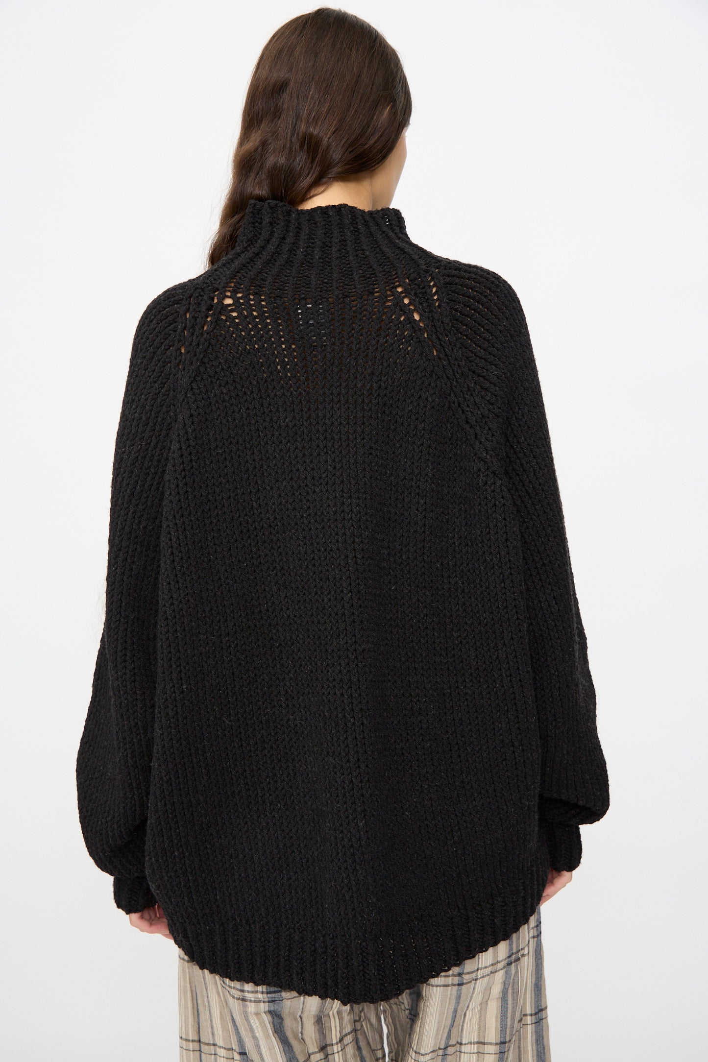 Person with long brown hair wears the Jan-Jan Van Essche Lalin Knit #68 Sweater in Pitch Black and plaid pants, shown from the back against a plain white background.