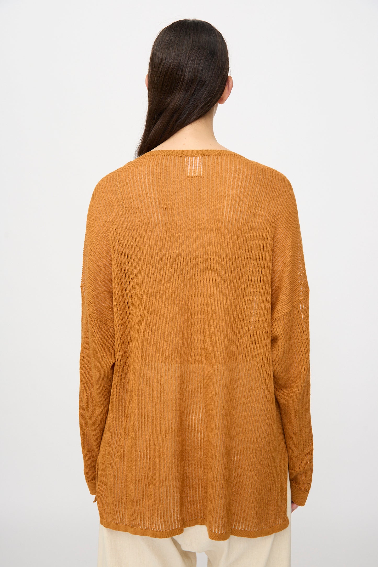 Person with long dark hair facing away, wearing the Jan-Jan Van Essche Linen Cotton Mesh Knit #76 in Orange over cream-colored pants, stands against a plain background.
