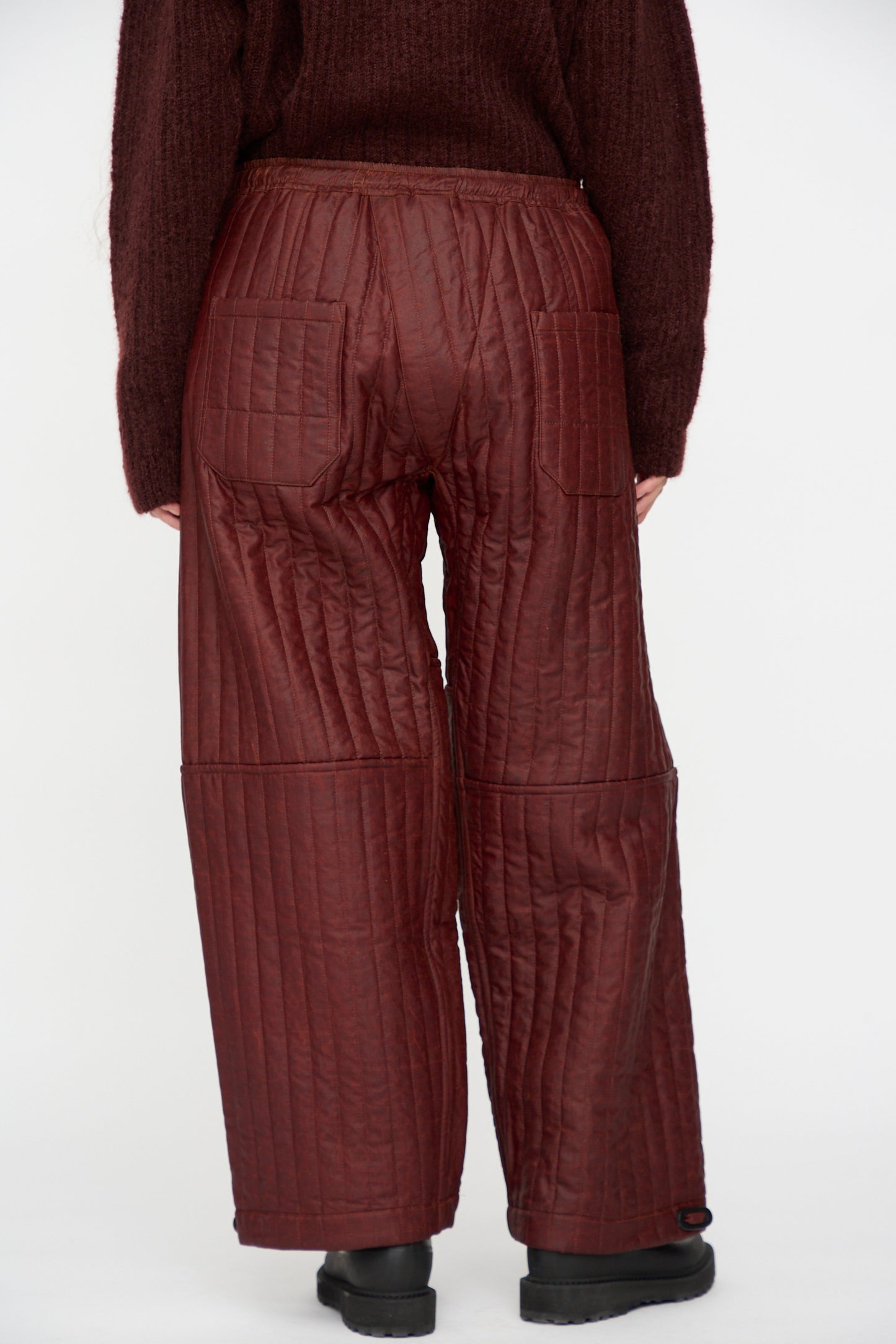 Person wearing Jan-Jan Van Essche Shuliang Silk Padded Trousers #89 in Oxblood, shown from the back with a matching sweater, standing against a plain white background.