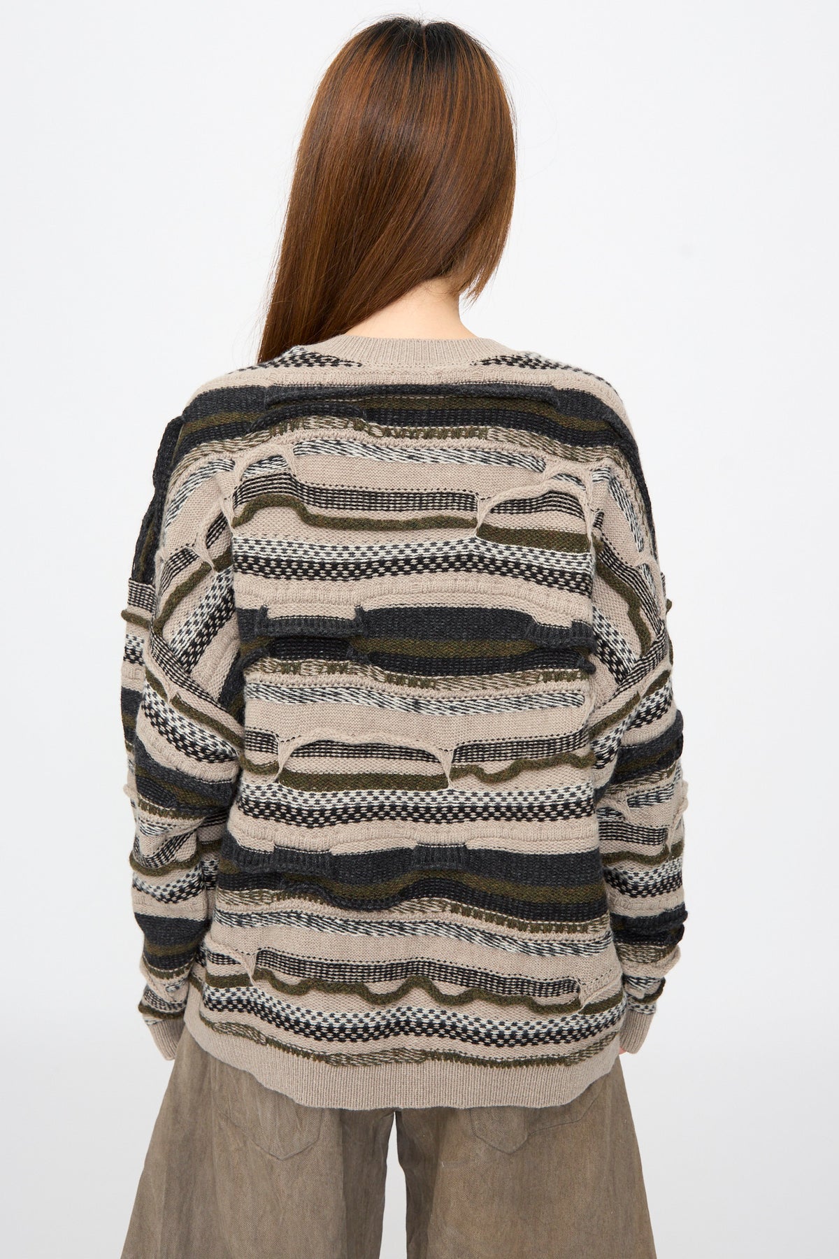 Back view of a person wearing a Jan-Jan Van Essche Super Fine Wool Knit Sweater #80 in Light Variation, featuring an oversized fit and multi-textured horizontal stripes in beige, black, and olive green.