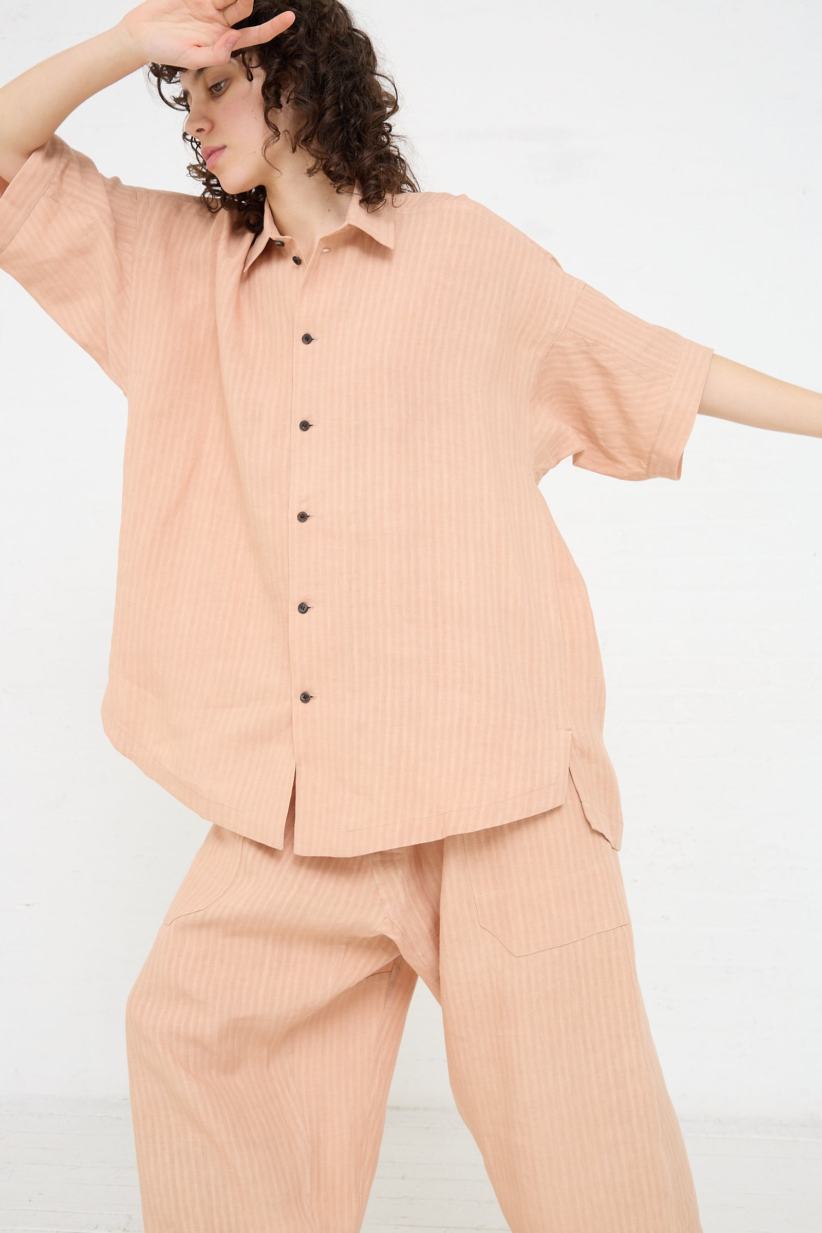 A woman wearing a pink Jan-Jan Van Essche Woven Linen Shirt in Ume and relaxed-fit pants.