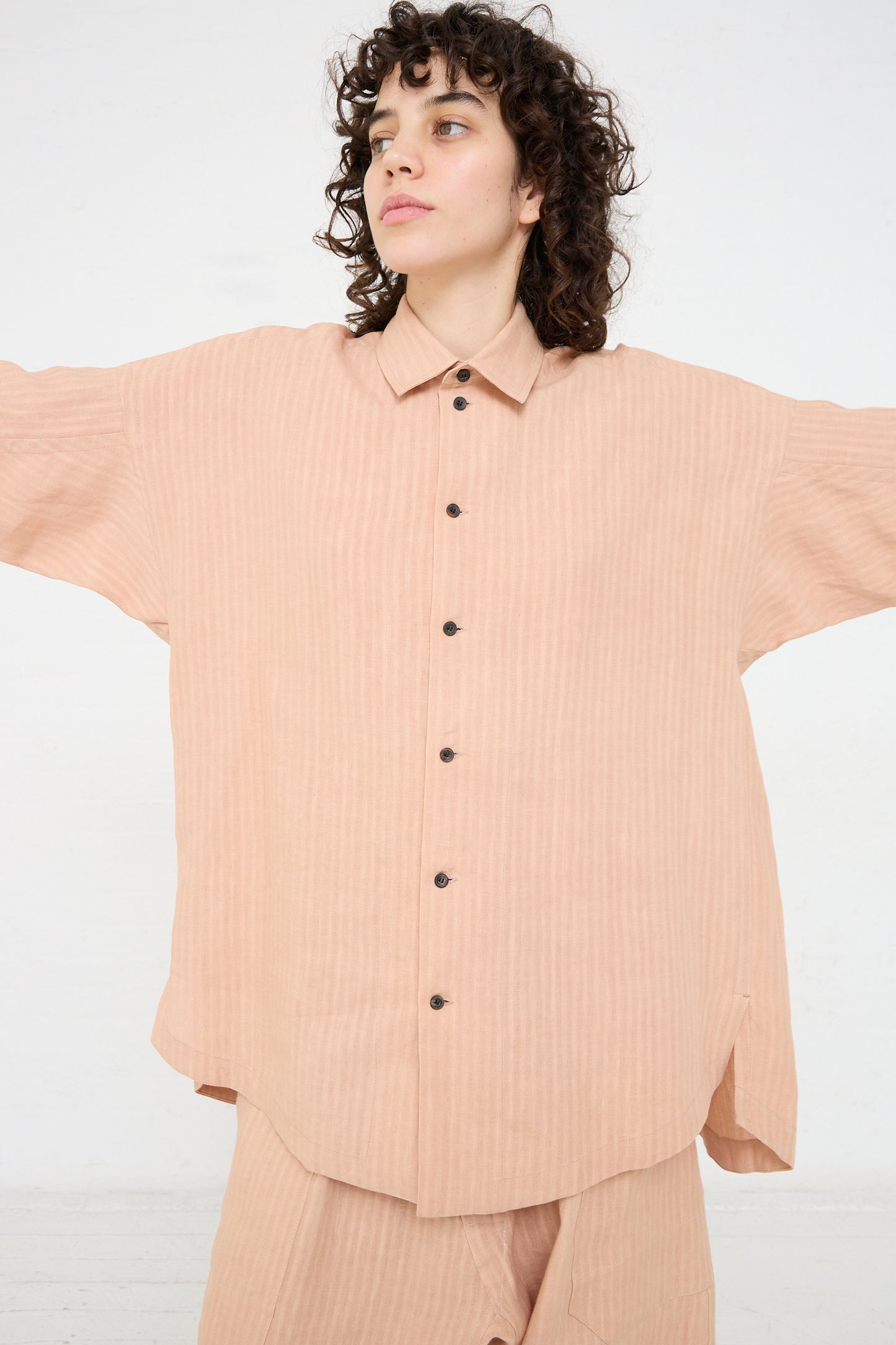 The model is wearing a relaxed fit peach Woven Linen Shirt in Ume and pants by Jan-Jan Van Essche.