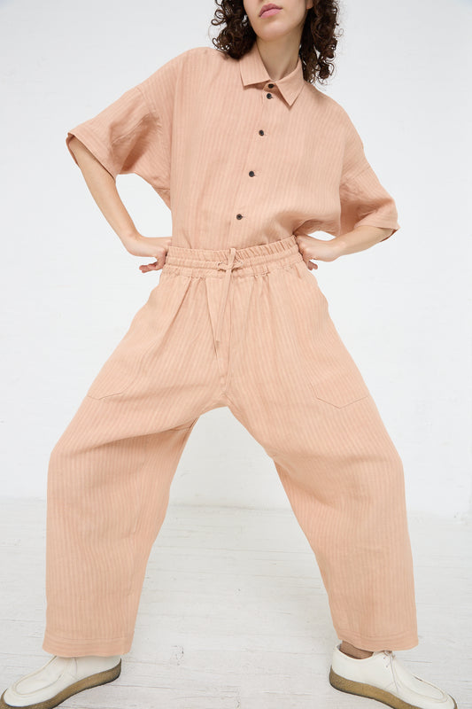 The model is wearing an elasticated woven linen trouser in Ume (Pink) by Jan-Jan Van Essche.