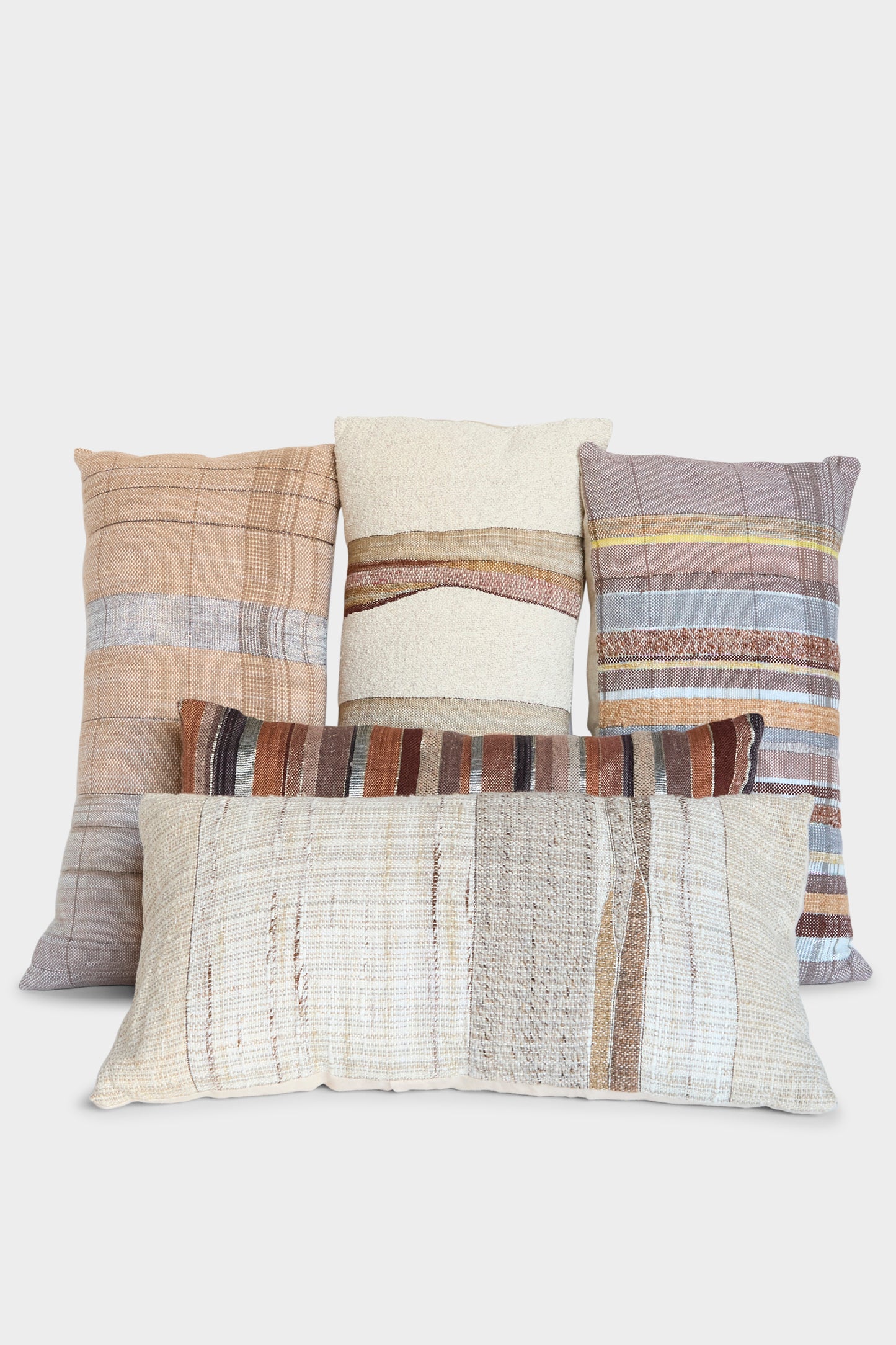 The Handmade Rock Slab Pillow in Neutral and Olive by Jess Feury is crafted in California from sustainable fibers, featuring striped and plaid designs in earthy tones, displayed against a white background.