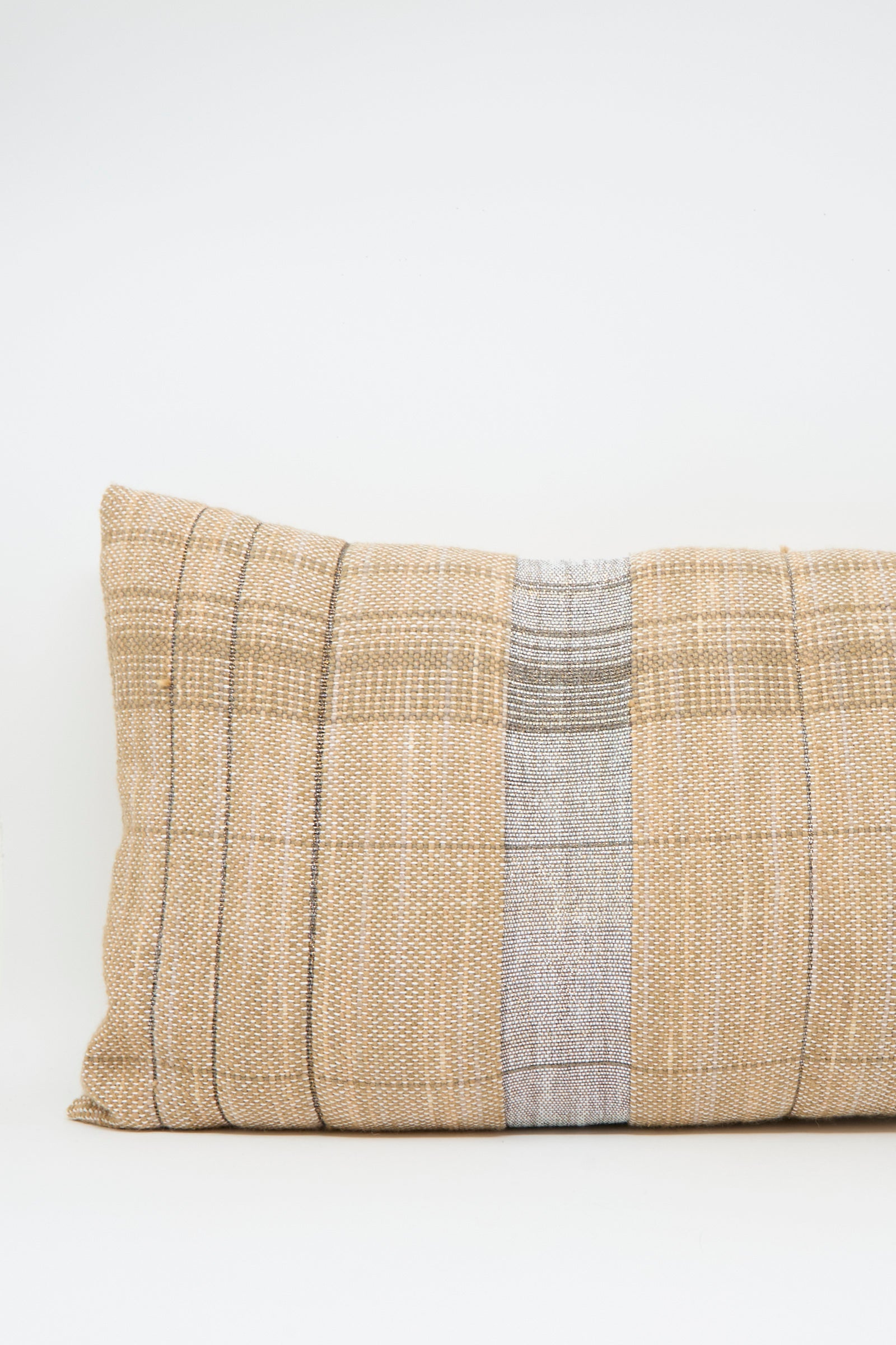 The Woven Pillow in Blush and Silver by Jess Feury features a rectangular handwoven design with a plaid pattern and central silver stripe, made from sustainable fibers and displayed on a plain white background.