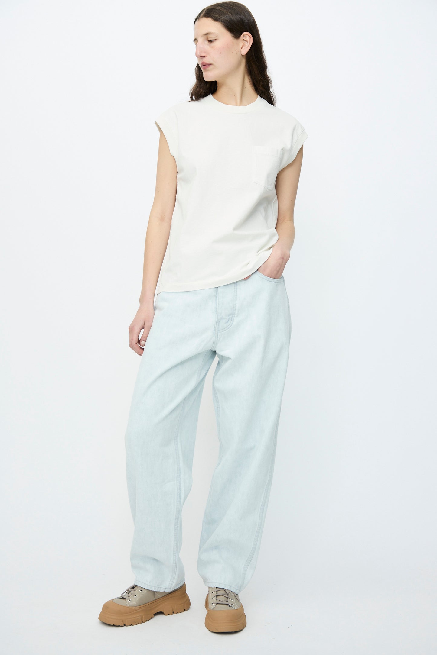Person in a white sleeveless top, Jesse Kamm's Japanese Denim California Wide in Pale Blue jeans, and tan shoes, standing against a plain white background.