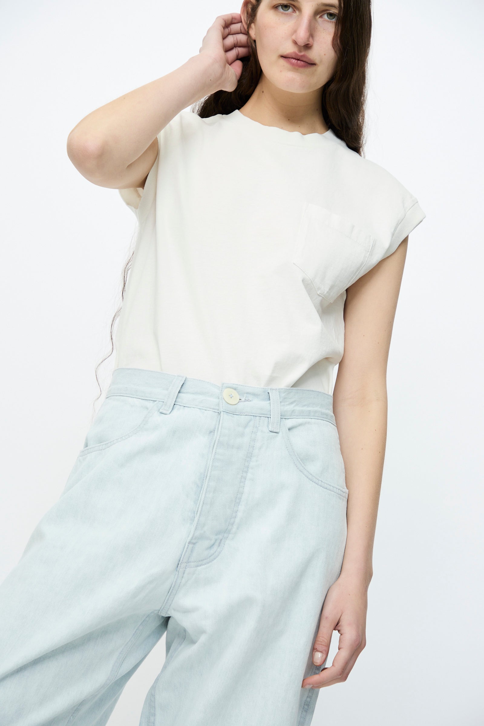 A person with long hair is wearing a relaxed-fit white sleeveless top and Jesse Kamm's Japanese Denim California Wide in Pale Blue jeans, standing against a plain white background.