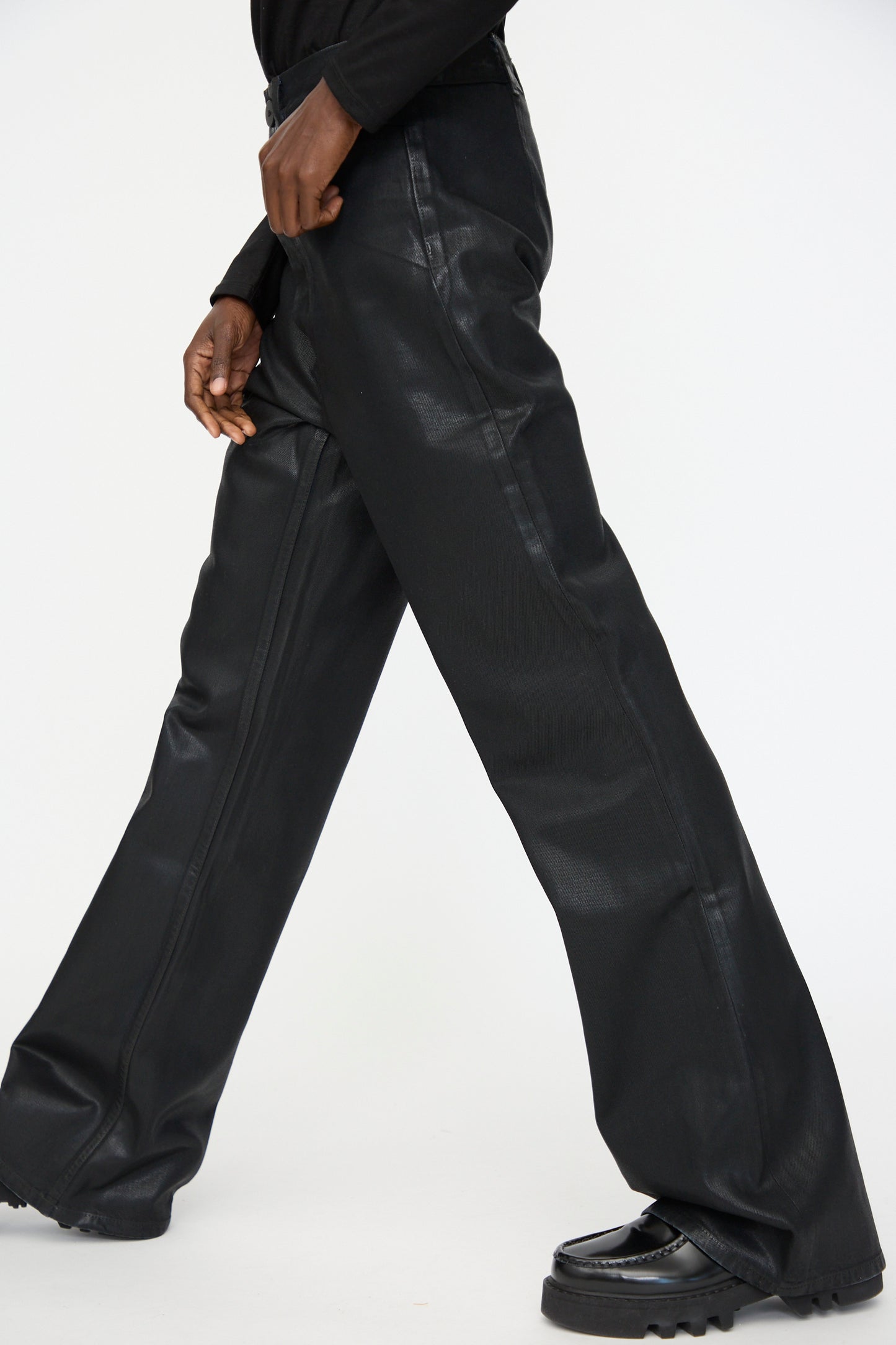 A person wears Jesse Kamm's Japanese Denim Les Deux Pants in Black Lacquer with black shoes, walking against a plain white background.
