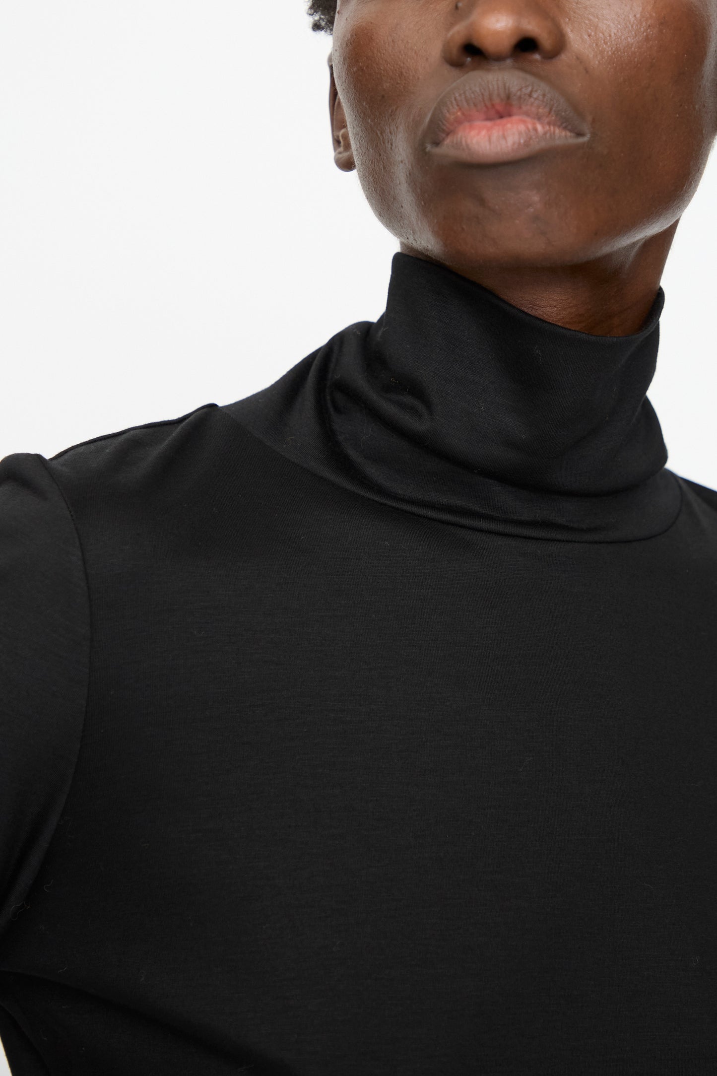 A person wearing the Jesse Kamm Japanese Organic Cotton Classic Turtleneck in Black is shown from the shoulders up against a plain white background.