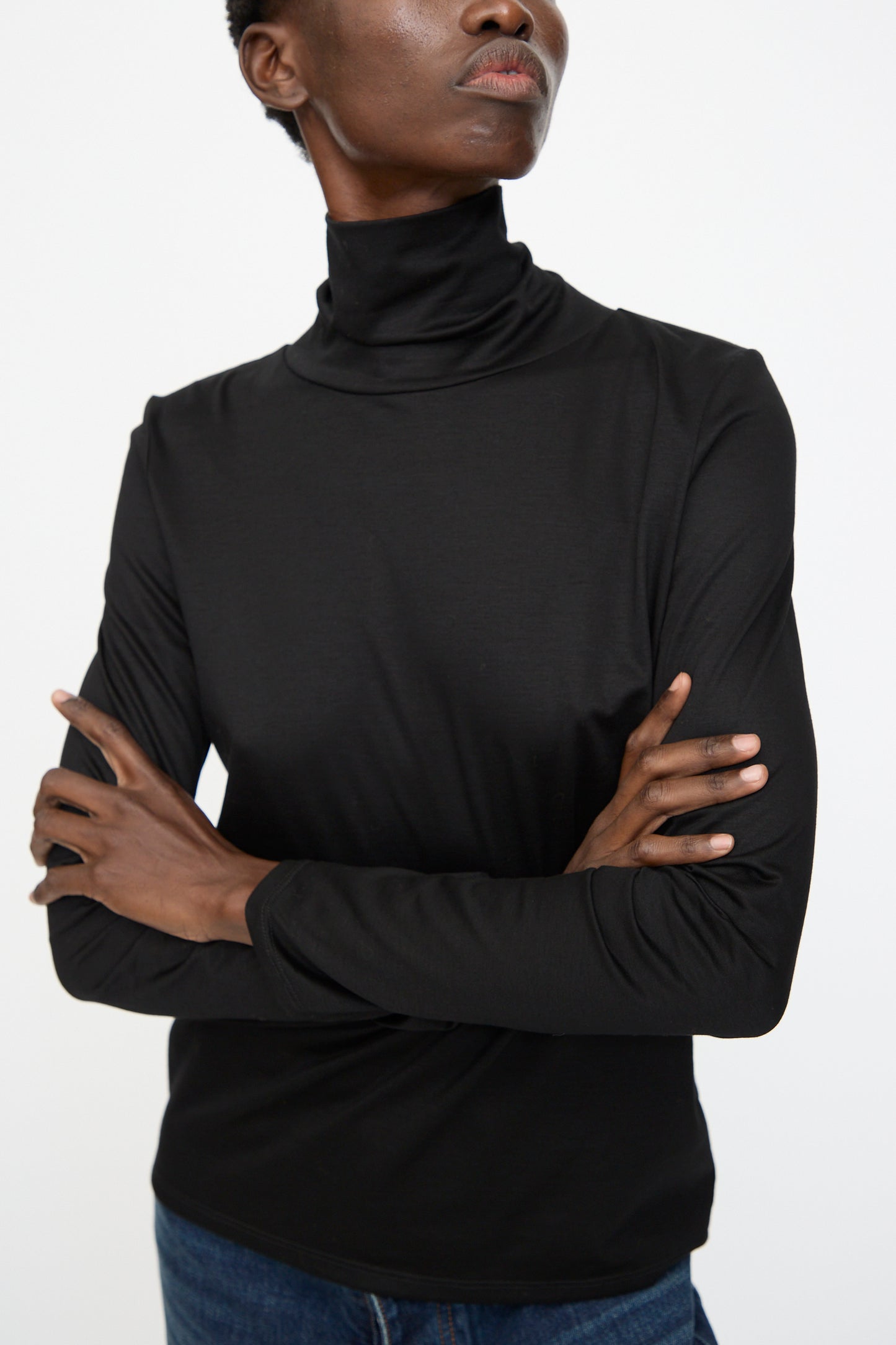 A person wearing the Jesse Kamm Japanese Organic Cotton Classic Turtleneck in Black, arms crossed, shown from shoulders to waist against a plain background.
