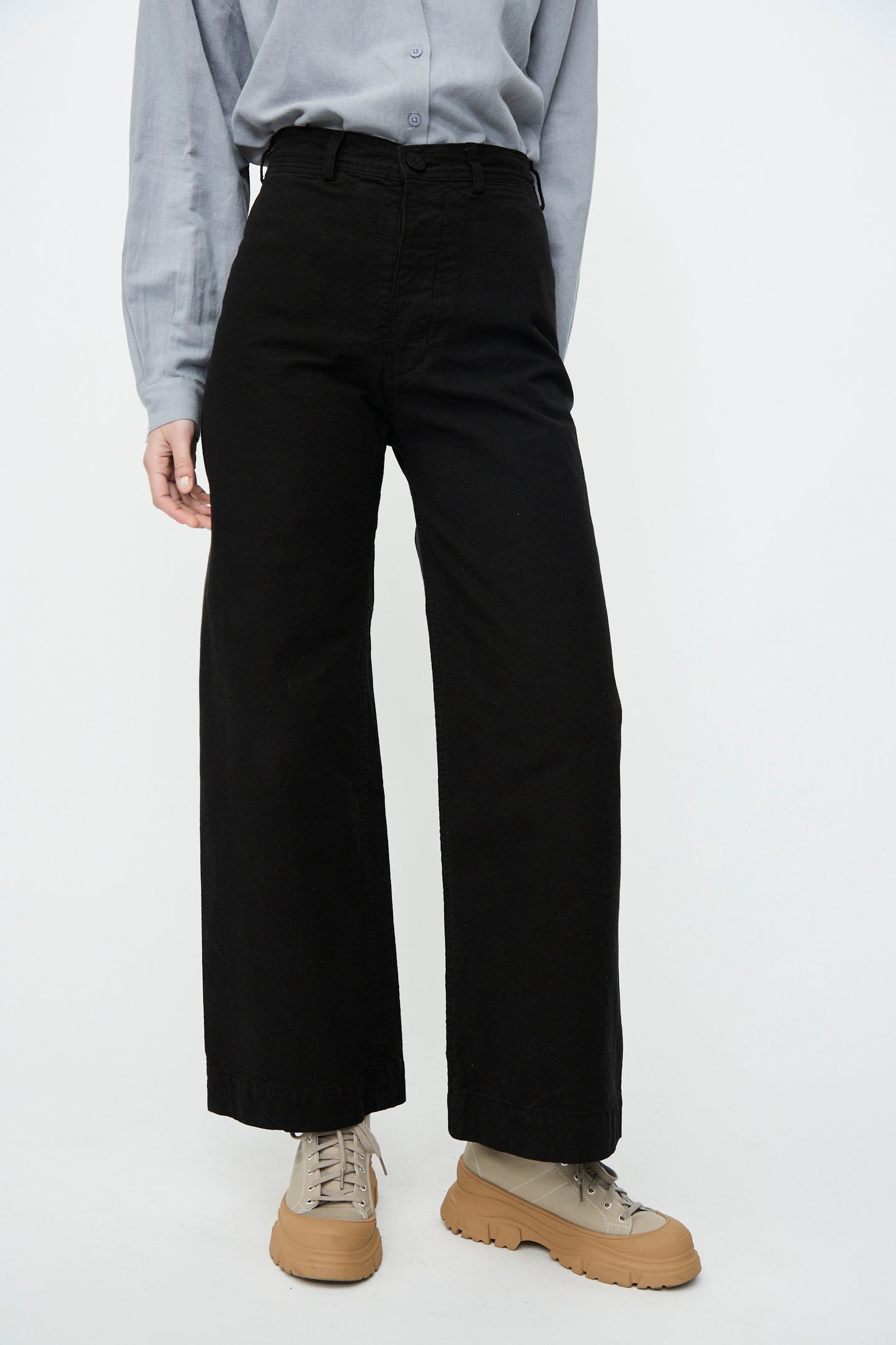 A model in a light blue shirt tucked into Jesse Kamm Sailor Pant in Black and tan platform shoes stands against a white background.