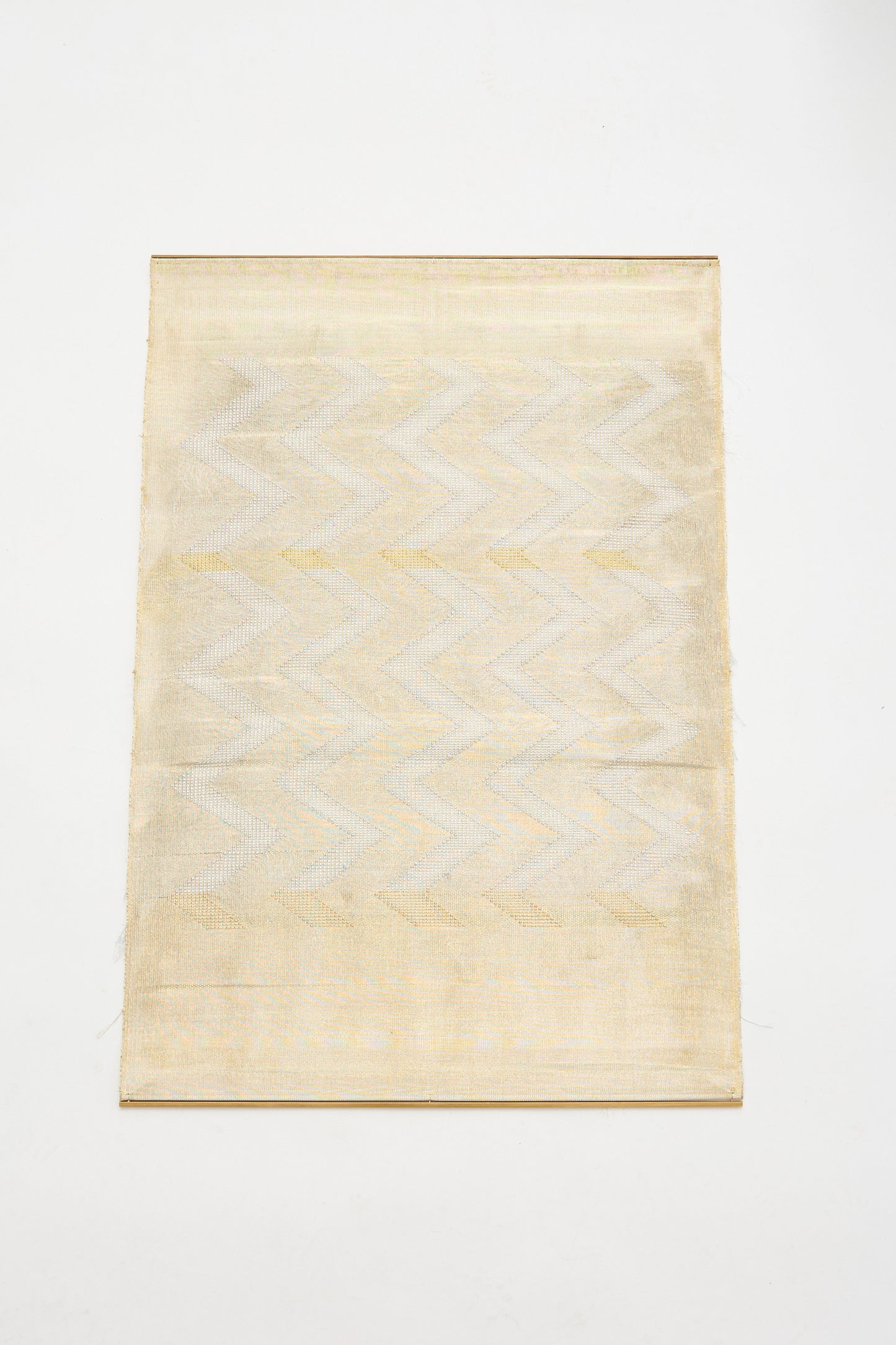 The Great Awakener Weaving by Justine Ashbee is a rectangular beige textile featuring a subtle zigzag pattern with metallic fibers, displayed flat on a white background.