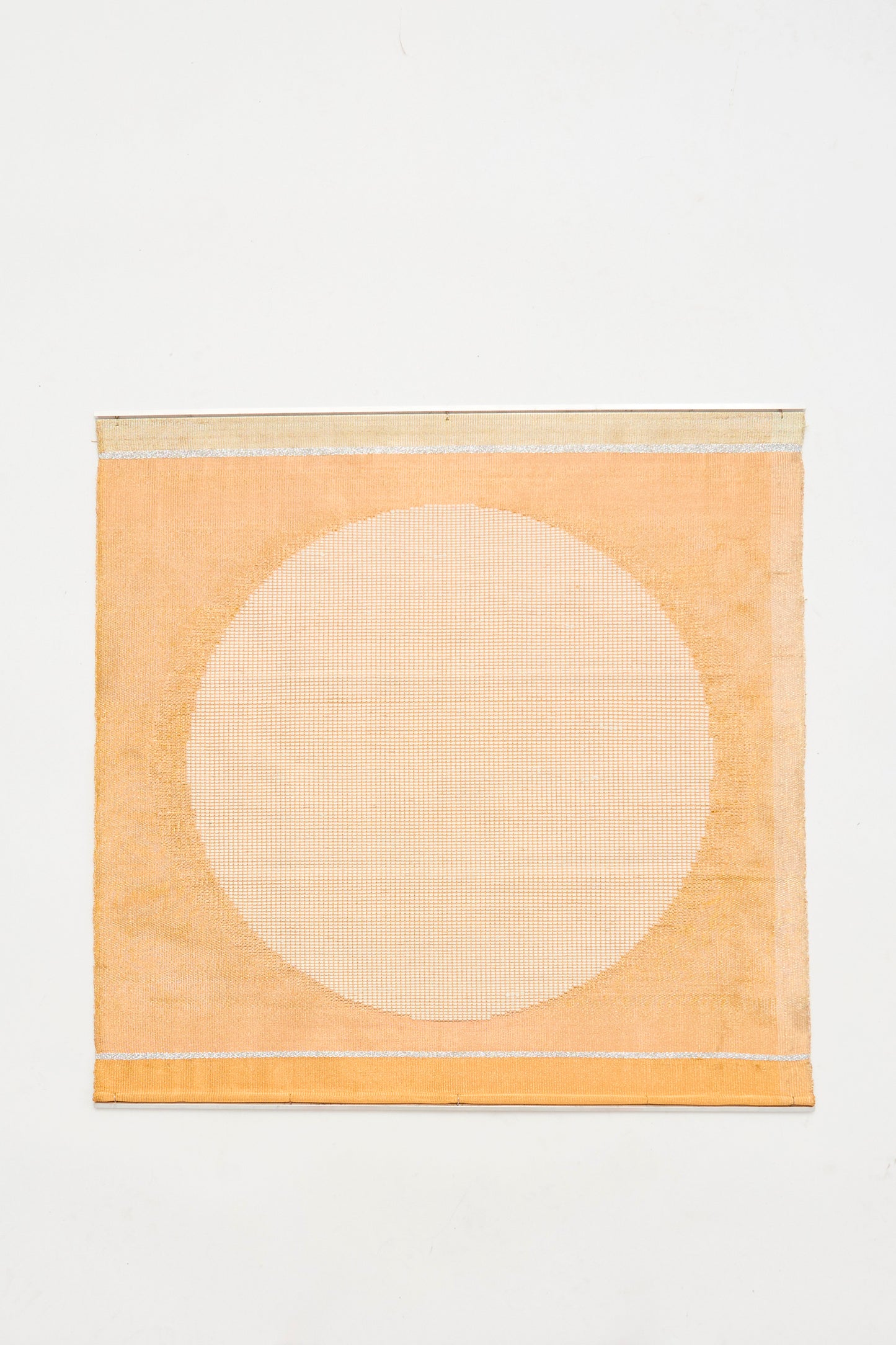 The White Moon Weaving by Justine Ashbee is a handmade UK wall hanging in light orange, showcasing a large, pale circle centered on a plain white background.