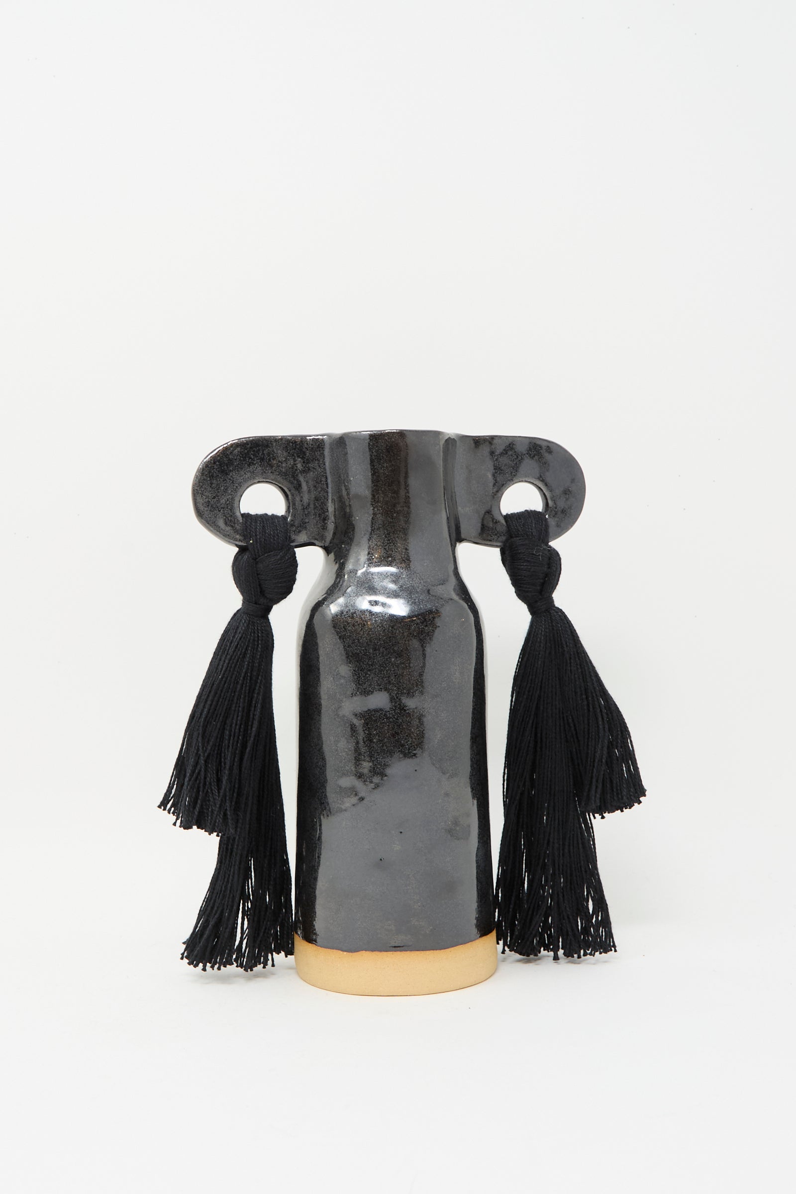 Karen Tinney’s Vase #606 in Black is a handmade black stoneware vase with a wide horizontal top and two large black tassels on each side, displayed against a plain white background.