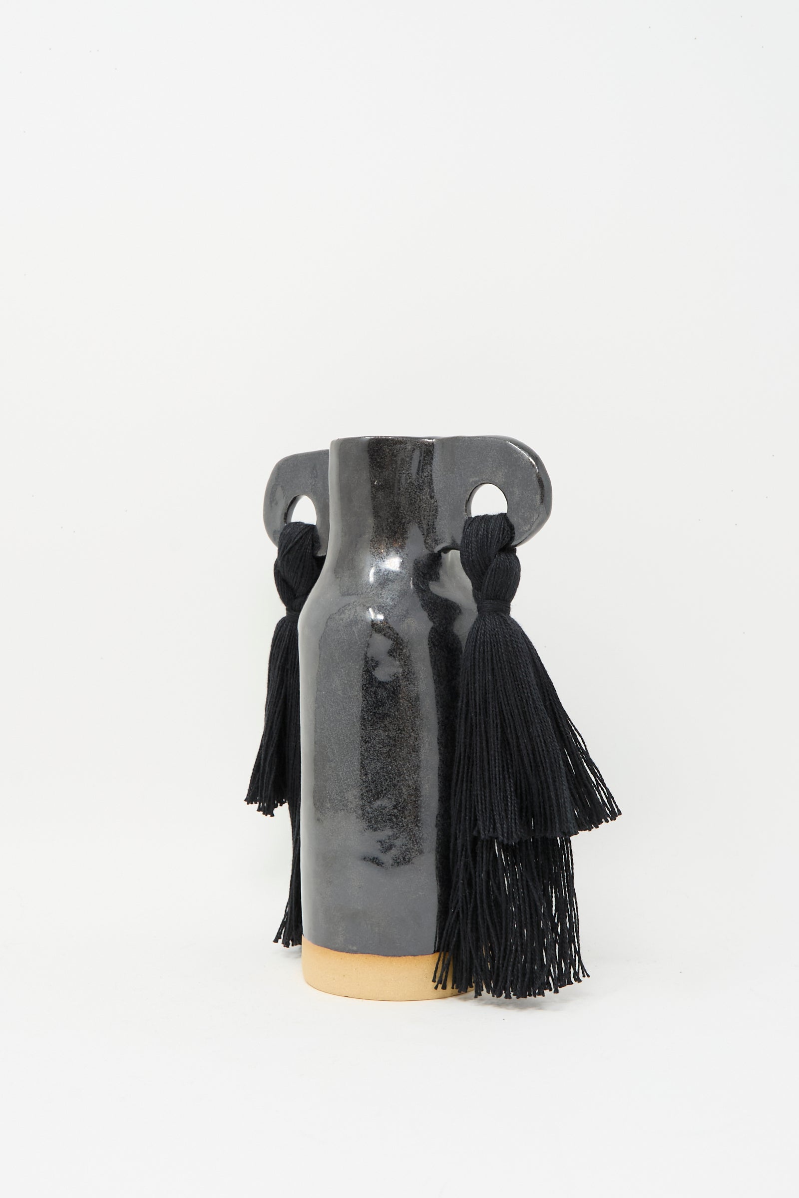 Karen Tinney’s Vase #606 in Black, a glossy stoneware vase with two circular handles featuring long black tassels, is displayed on a plain white background.