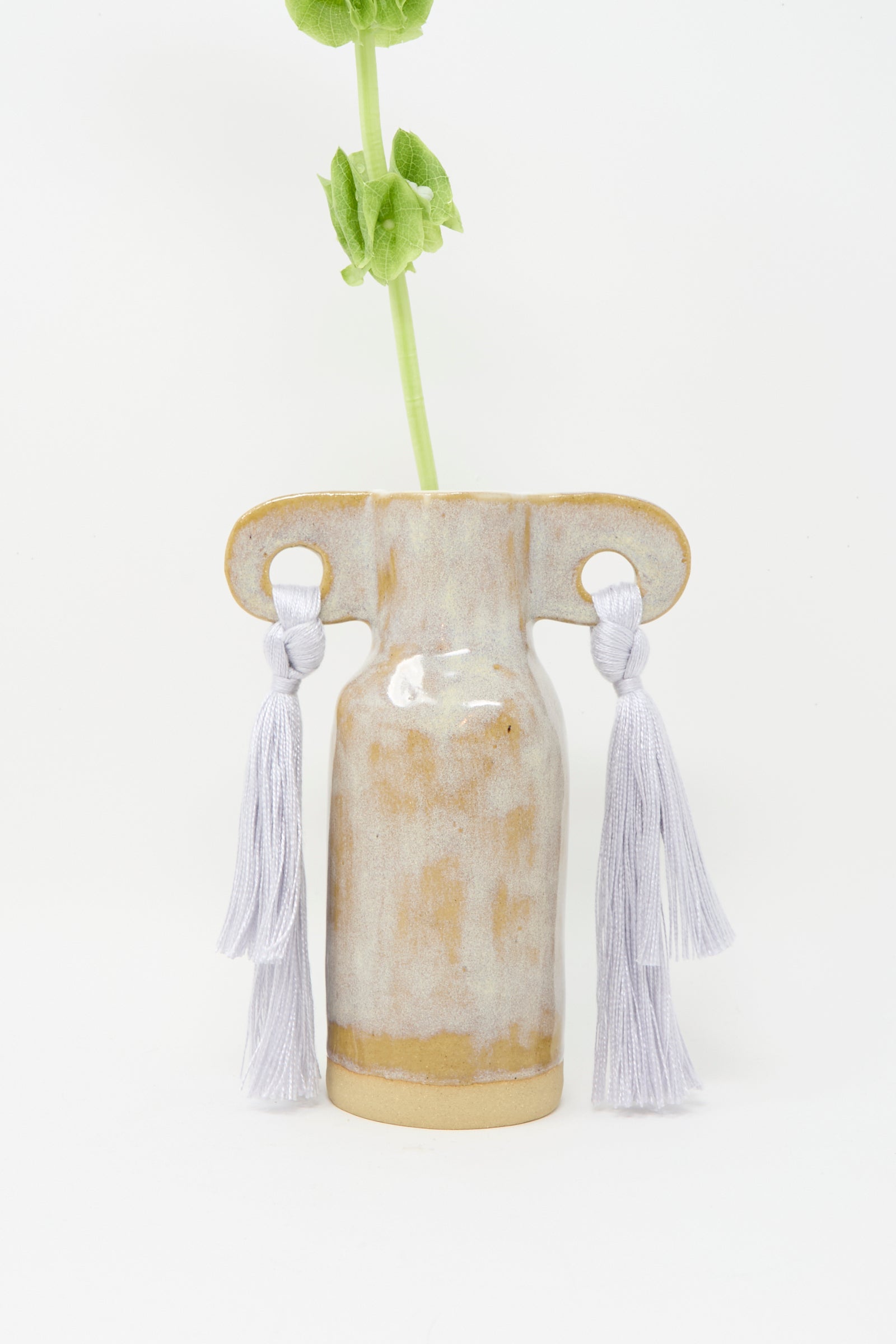 The Karen Tinney Vase #606 in Gray is a petite stoneware vase handmade in Vermont, featuring two looped handles with gray tencel fringe. Shown against a white background, it displays a single green stem.