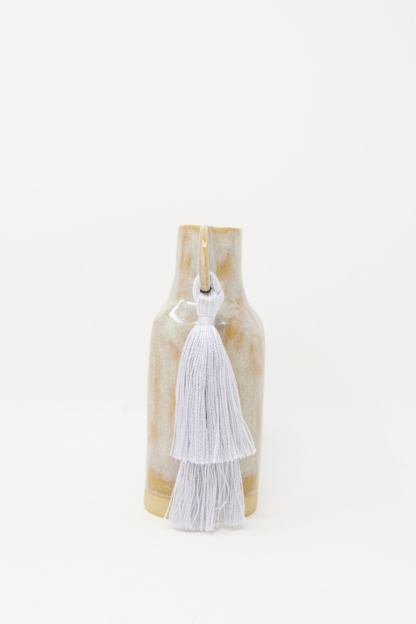 Karen Tinney’s Vase #606 in Gray is a petite, handmade stoneware vase with a glossy beige finish and gray tencel fringe at the neck, crafted in Vermont and shown against a plain white background.