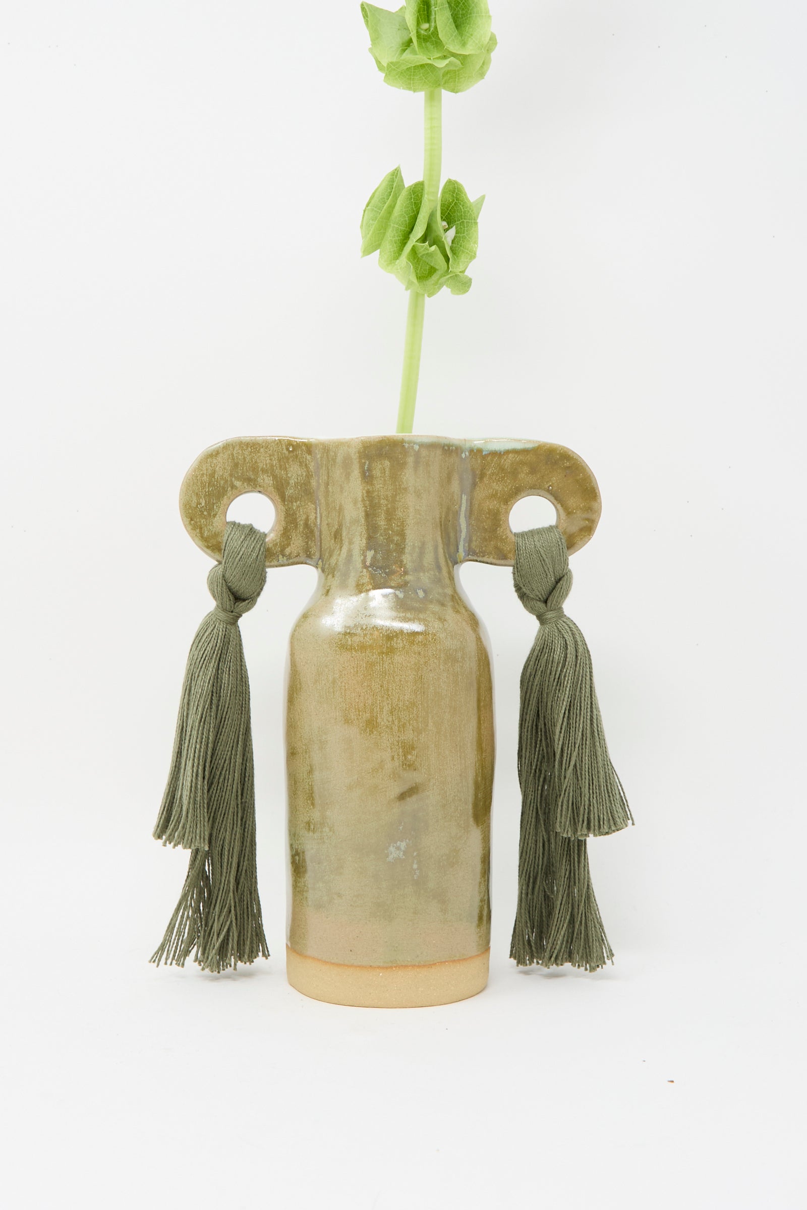 Vase #606 in Olive by Karen Tinney is a petite handmade stoneware piece with two looped handles featuring green tassels, an olive glaze, and a green flower stem, displayed against a white background.