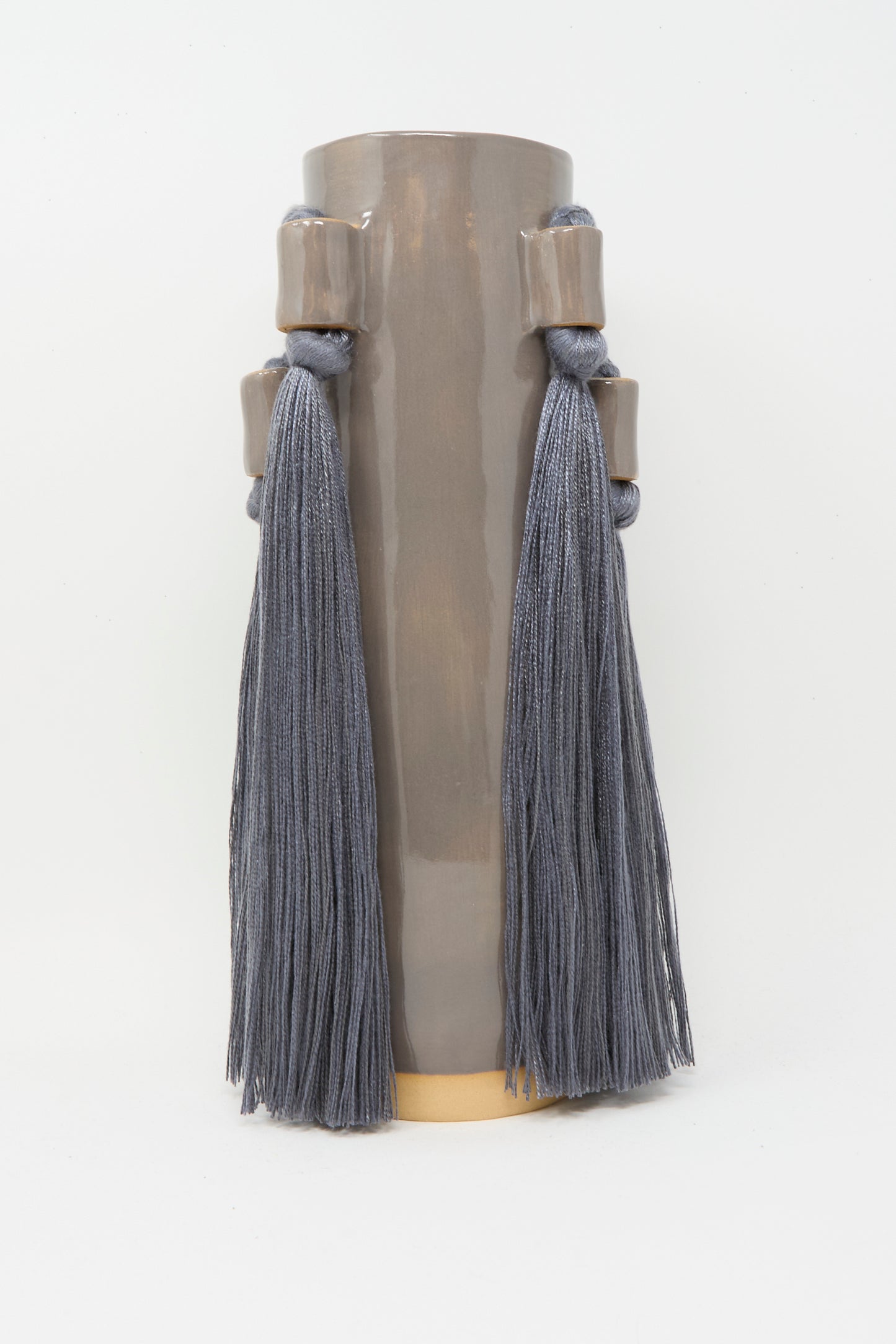 Karen Tinney Vase #735 in Charcoal is a tall, cylindrical, glossy stoneware piece with two large gray tassels, handmade and inspired by Vermont pottery traditions.