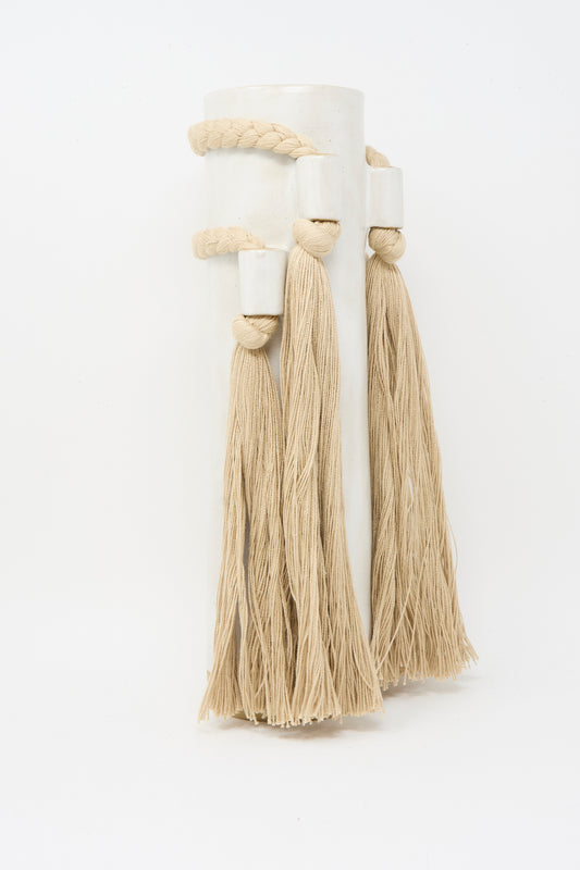 The Karen Tinney Vase #735 in White is handmade in Vermont, featuring two long beige tassels and a thick braided rope handle for an artisanal touch.