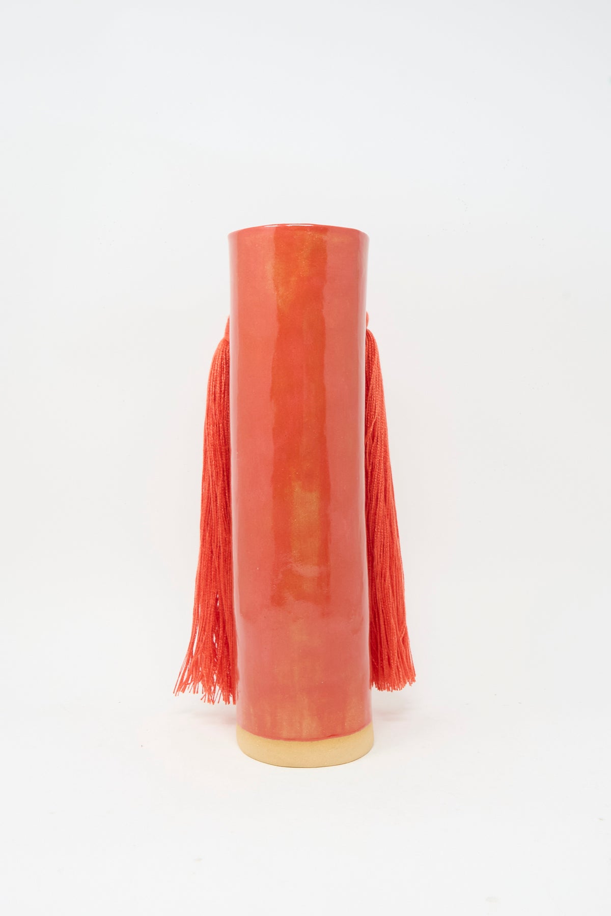 Vase #531 in Red by Karen Tinney is a tall, cylindrical red ceramic vase featuring long red tassels on each side.