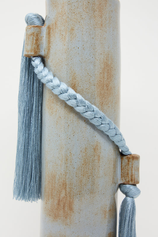 Blue tassel and cord wrapped around a weathered cylindrical Karen Tinney Vase #695 in Blue.