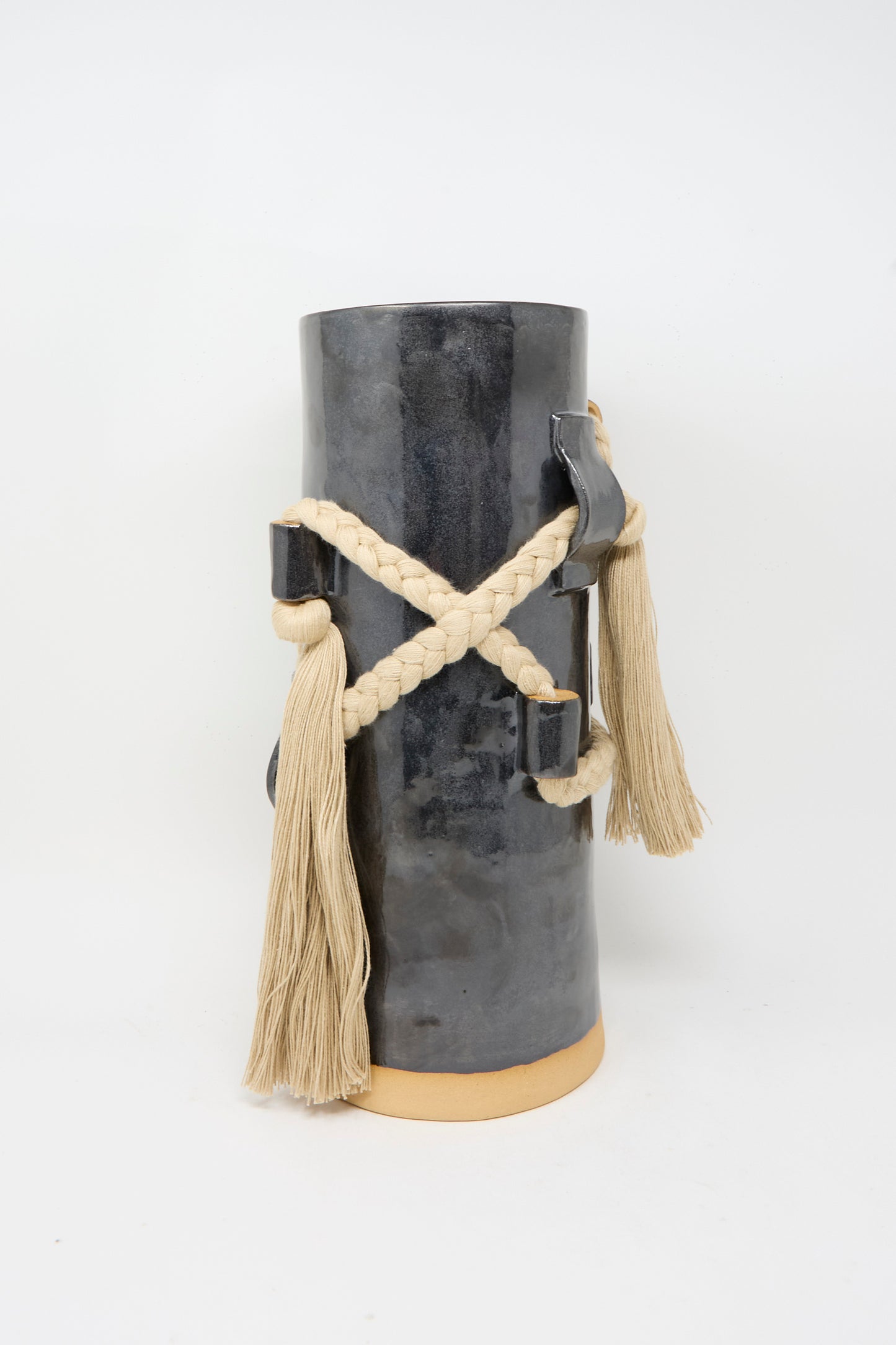 Vase #846 in Black and Tan by Karen Tinney is a tall, handcrafted stoneware vase featuring a glossy black glaze, complemented by braided cream rope and long tassels.