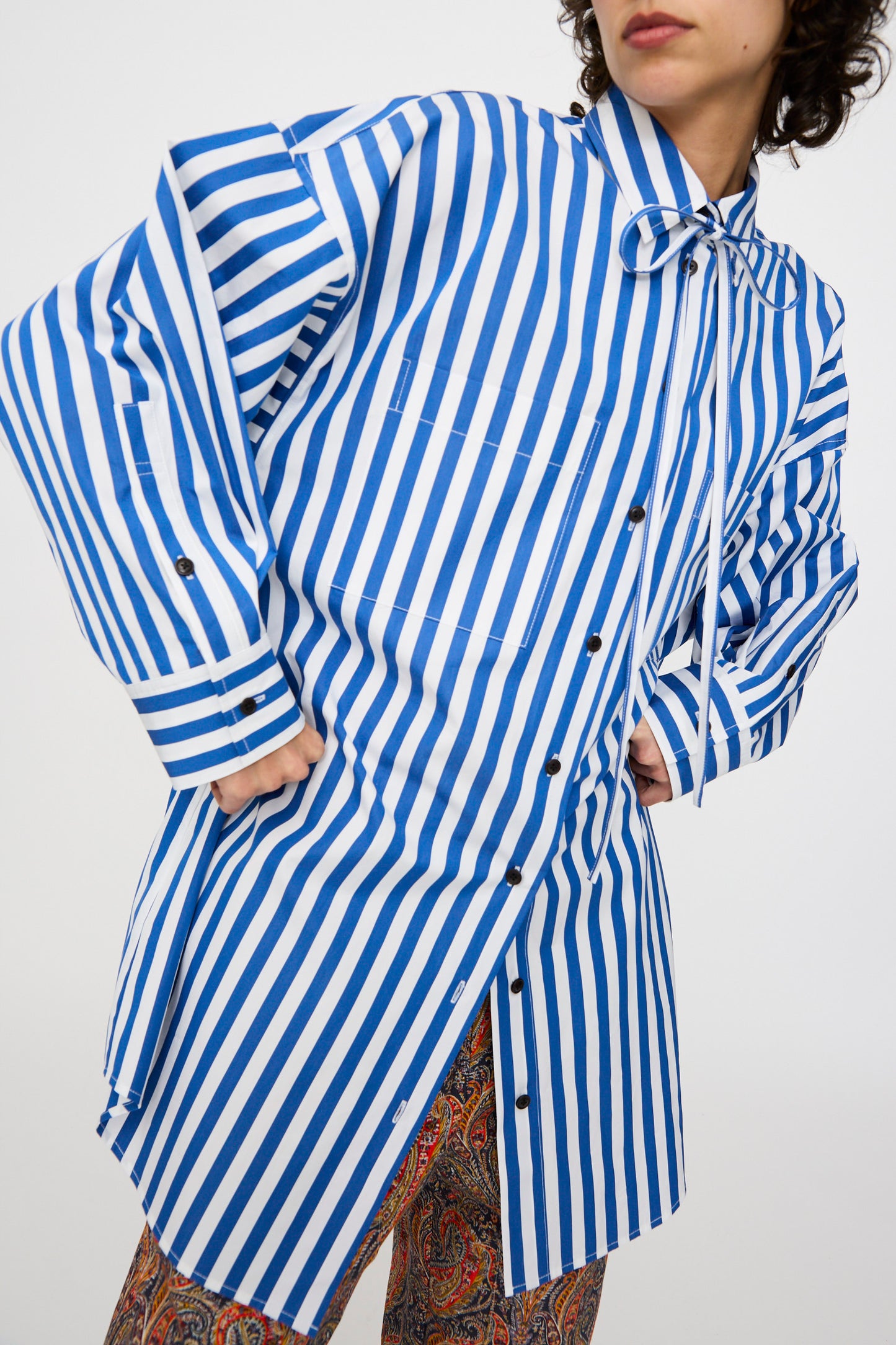 A person wearing the KasMaria Cotton Poplin Oversized Dress with Tie in Stripe with hands on their hips against a white backdrop.