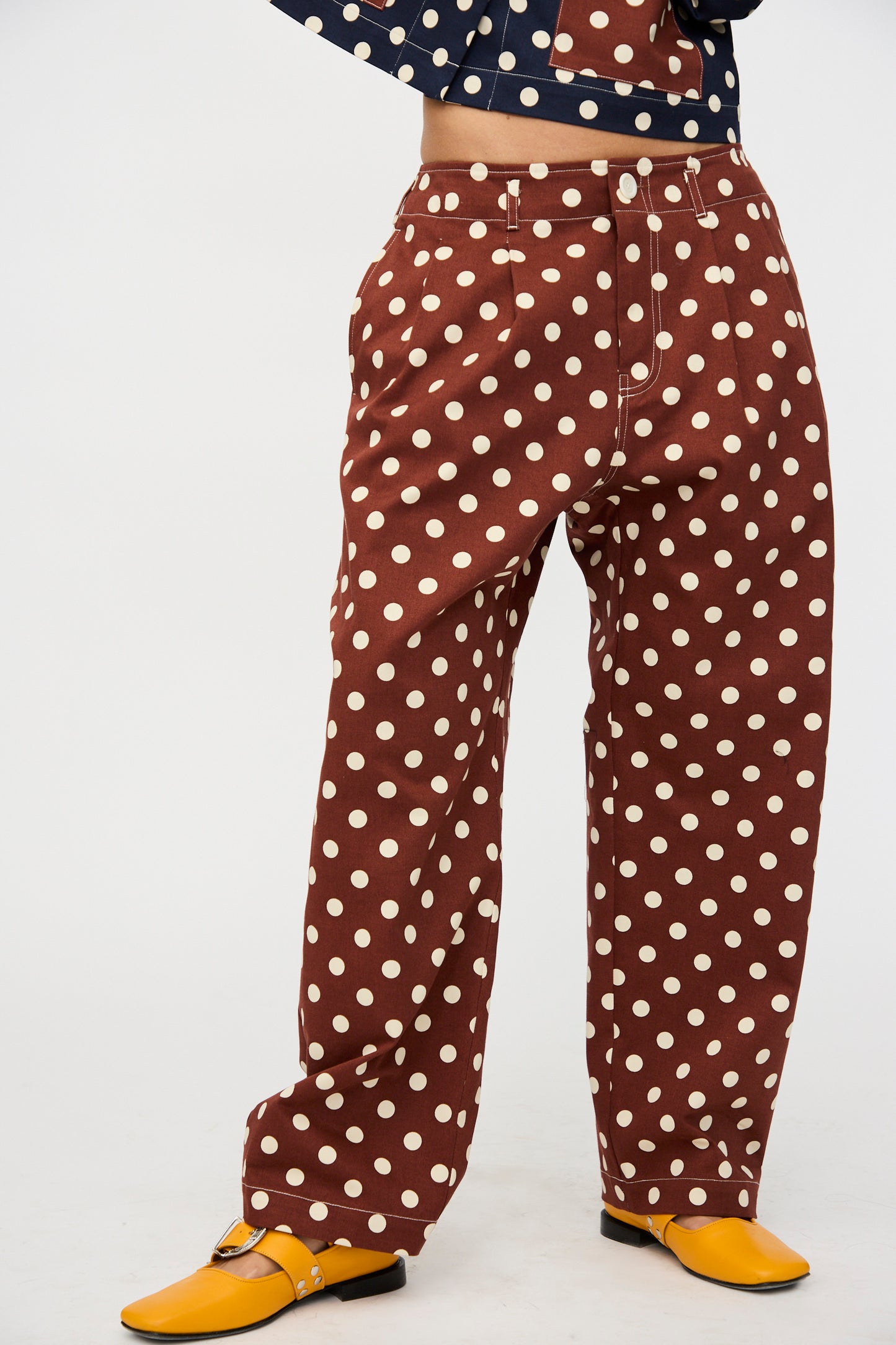Model shown from shoulders down wears KasMaria's Cotton Twill Pleated Trouser in Polka Dot with a matching top and yellow shoes, set against a plain background.