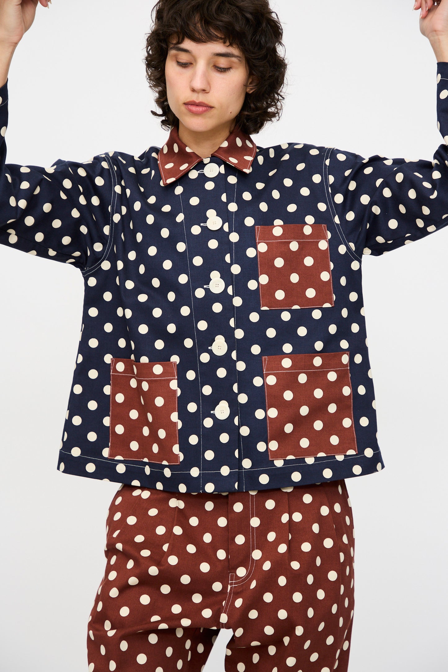 A person wears the KasMaria Cotton Twill Shirt Jacket in Polka Dot with contrasting brown patch pockets and matching brown polka dot pants, posing against a plain background.