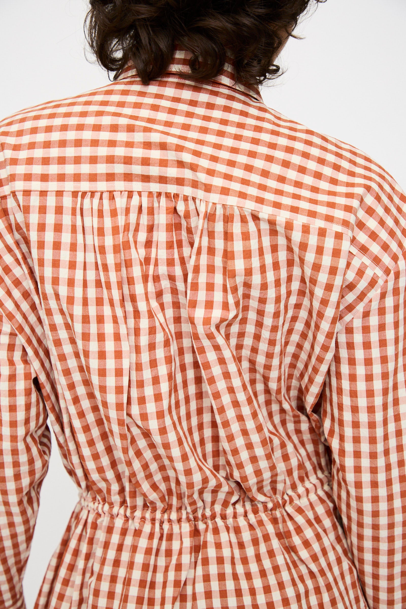 Close-up of a person wearing the KasMaria Crinkle Cotton Linen Drawstring Dress in red and white gingham, shown from the back with gathered fabric at the waist and upper back.