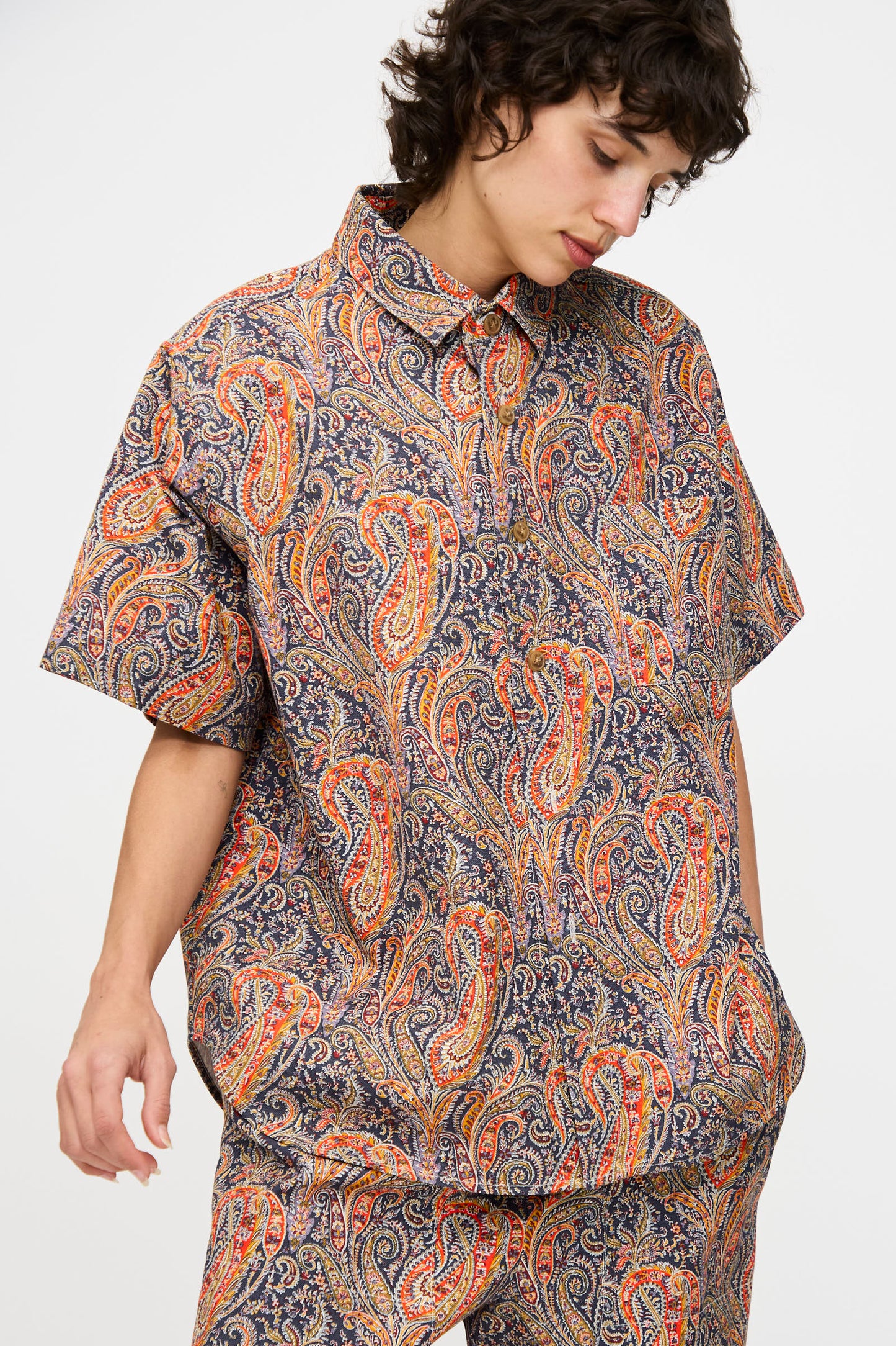 A person wears the KasMaria Liberty Cotton Canvas Shirt in Paisley and matching pants, standing against a plain white background and looking down.