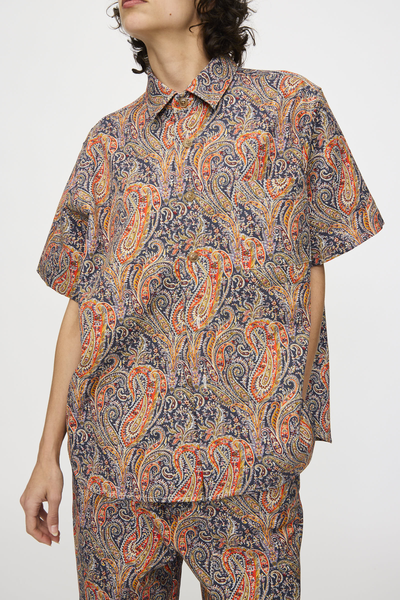A person wears the KasMaria Liberty Cotton Canvas Shirt in Paisley, a short-sleeved button-up made in NYC, paired with matching pants, standing against a plain background.