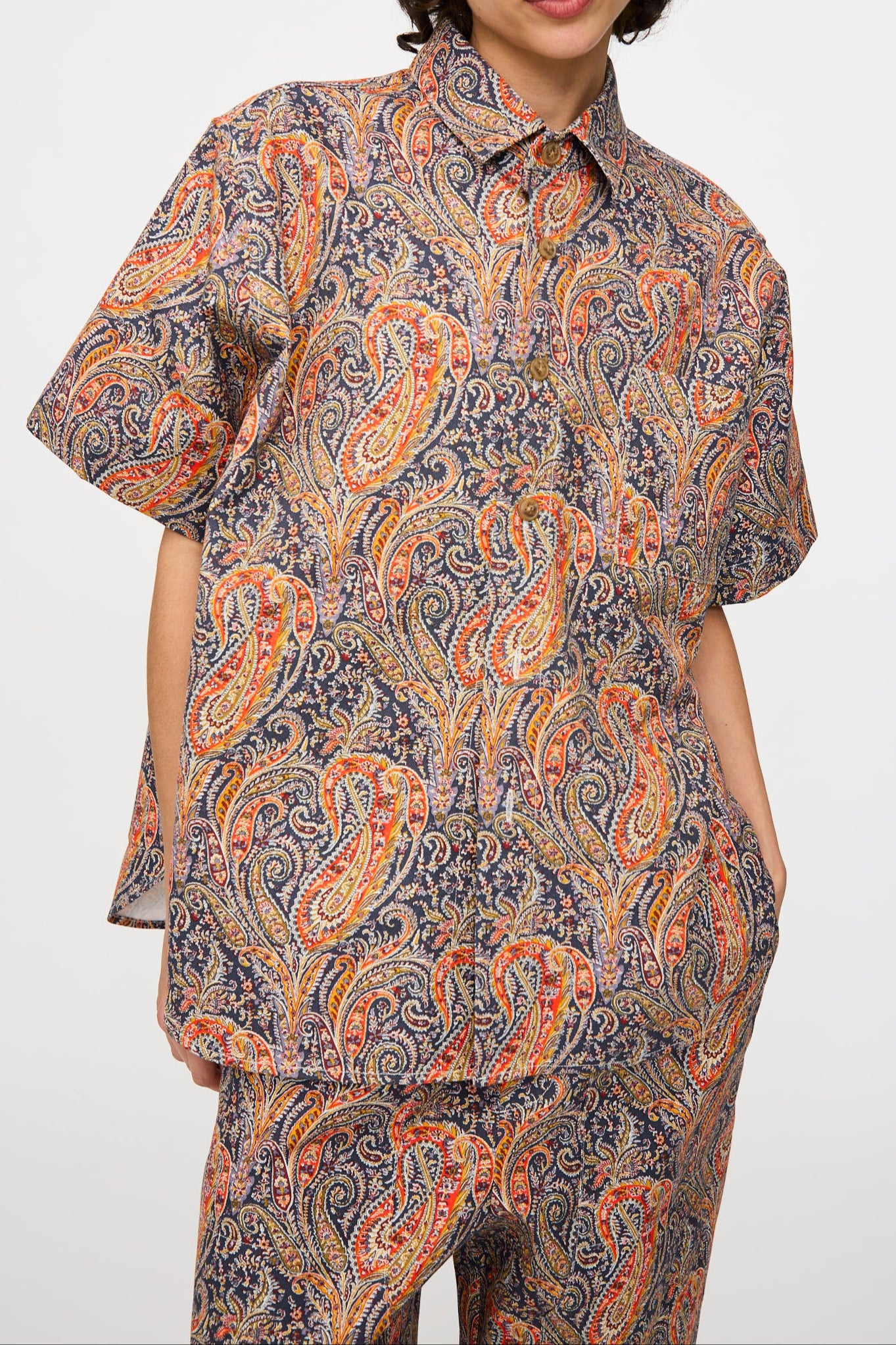A person wears the KasMaria Liberty Cotton Canvas Shirt in Paisley, paired with matching pants, standing against a plain white background.