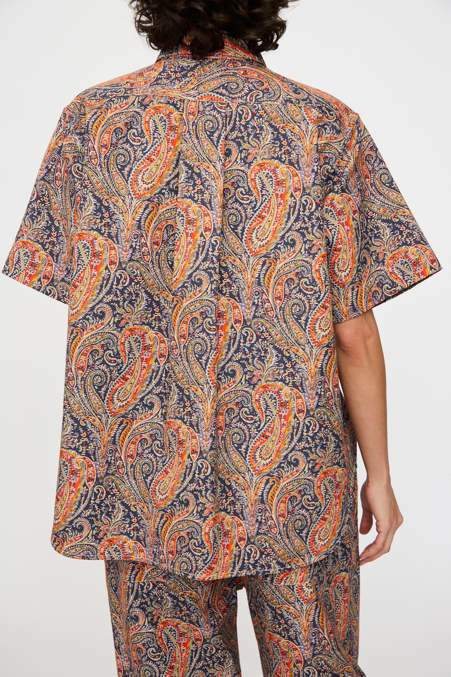 A person with dark curly hair is shown from the back, wearing the KasMaria Liberty Cotton Canvas Shirt in Paisley.