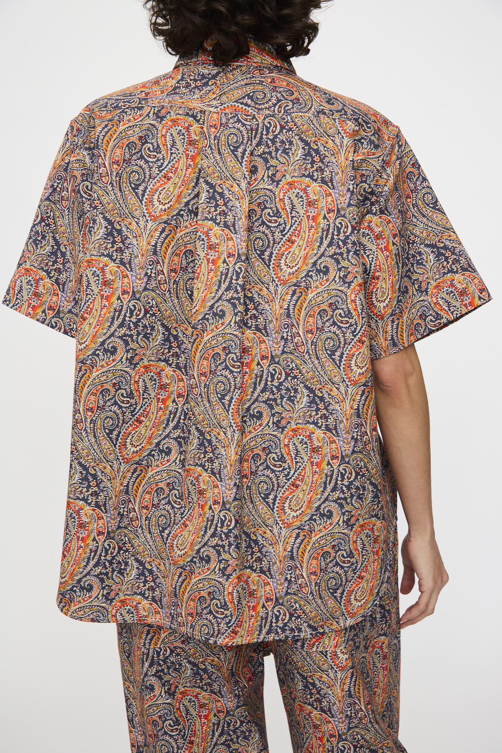 A person with dark curly hair is shown from the back, wearing the KasMaria Liberty Cotton Canvas Shirt in Paisley.