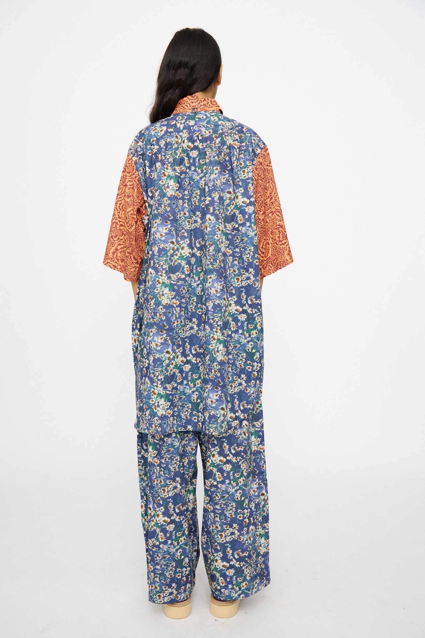 A person faces away in a KasMaria Liberty Floral Oversized Shirtdress in Blue and Orange, posing against a plain white background.