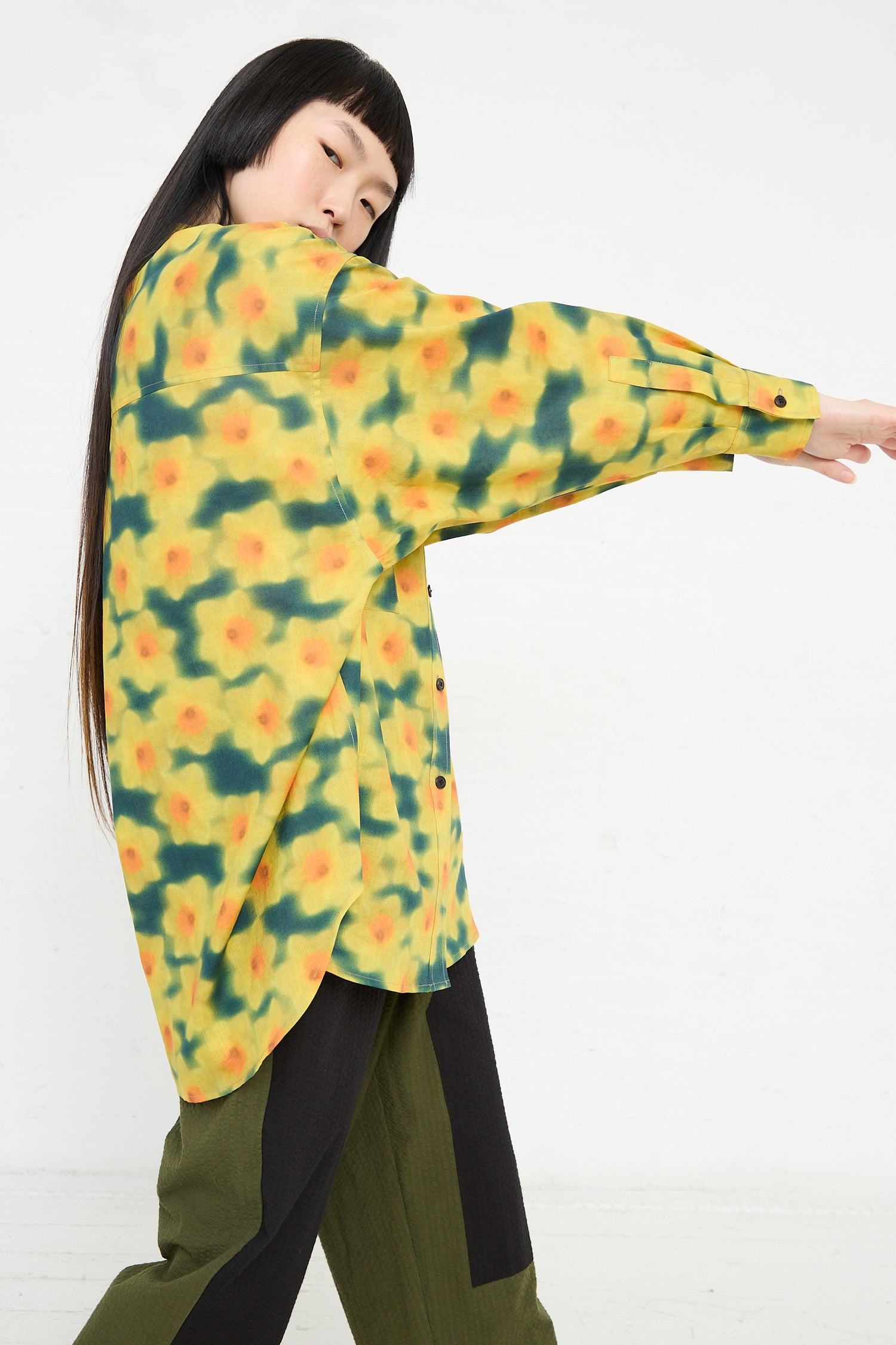 A woman in a KasMaria Cotton Linen Large Front Pocket Shirt in Daffodil Print extending her arm to the side against a white background.