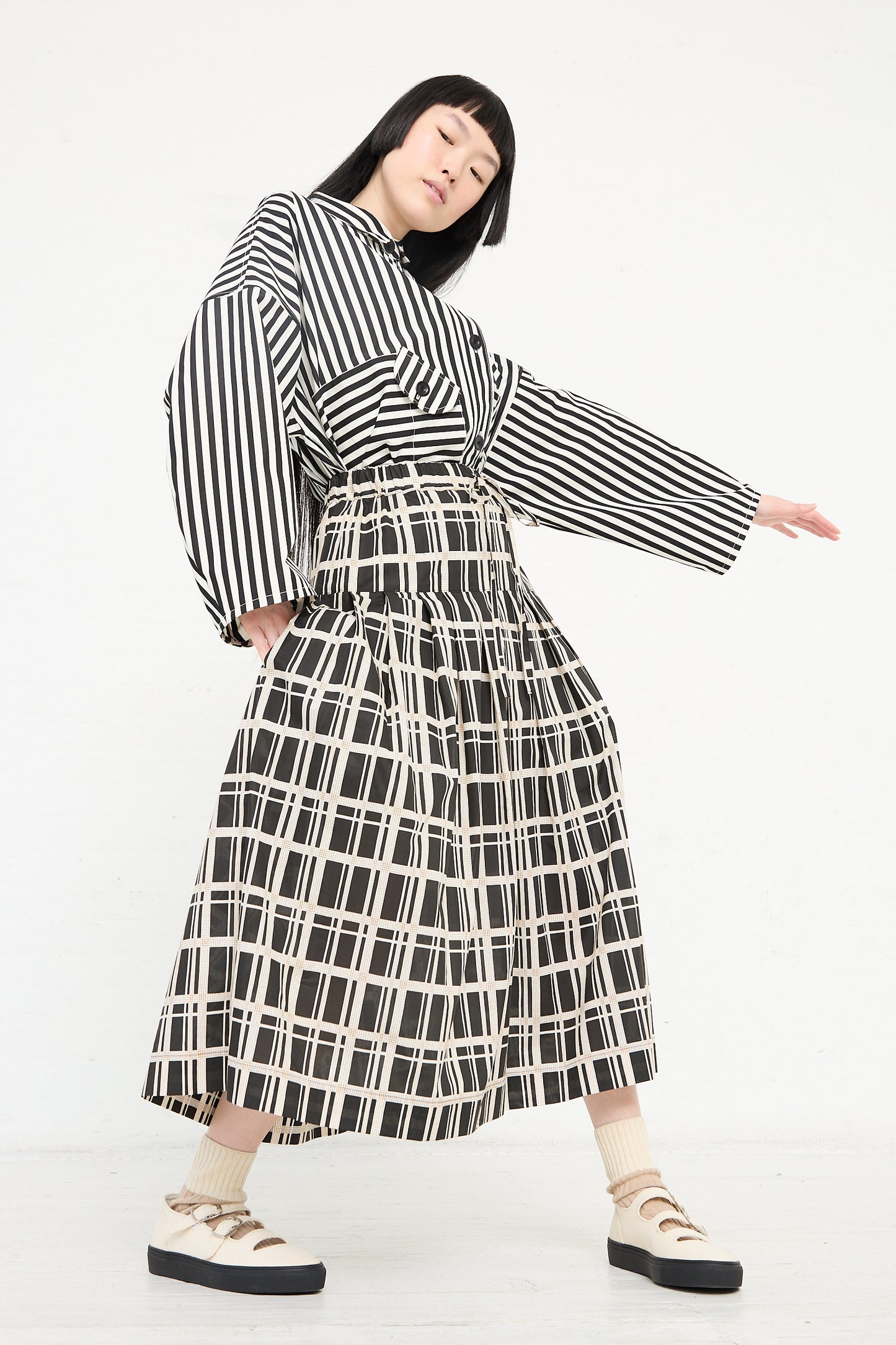 Woman posing in a KasMaria Cotton Pleated Long Skirt in Grid Print against a white background.