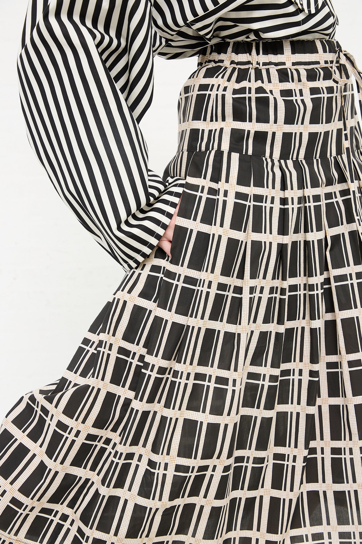 A close-up of a person wearing the KasMaria Cotton Pleated Long Skirt in Grid Print with a relaxed fit and grid print.