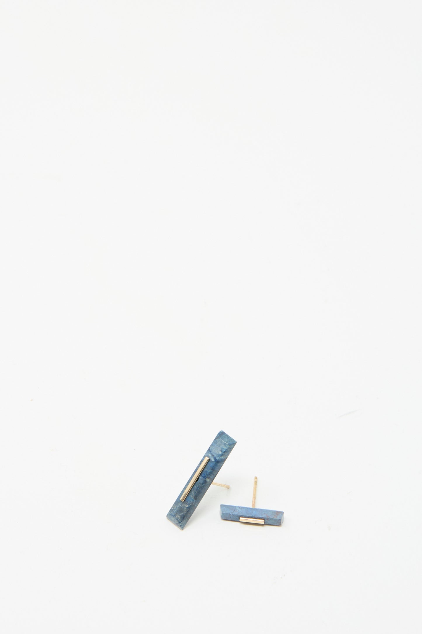 The Kathleen Whitaker 14K Yellow Gold Long Staple Studs, featuring Lapis stones, rest on a white surface.