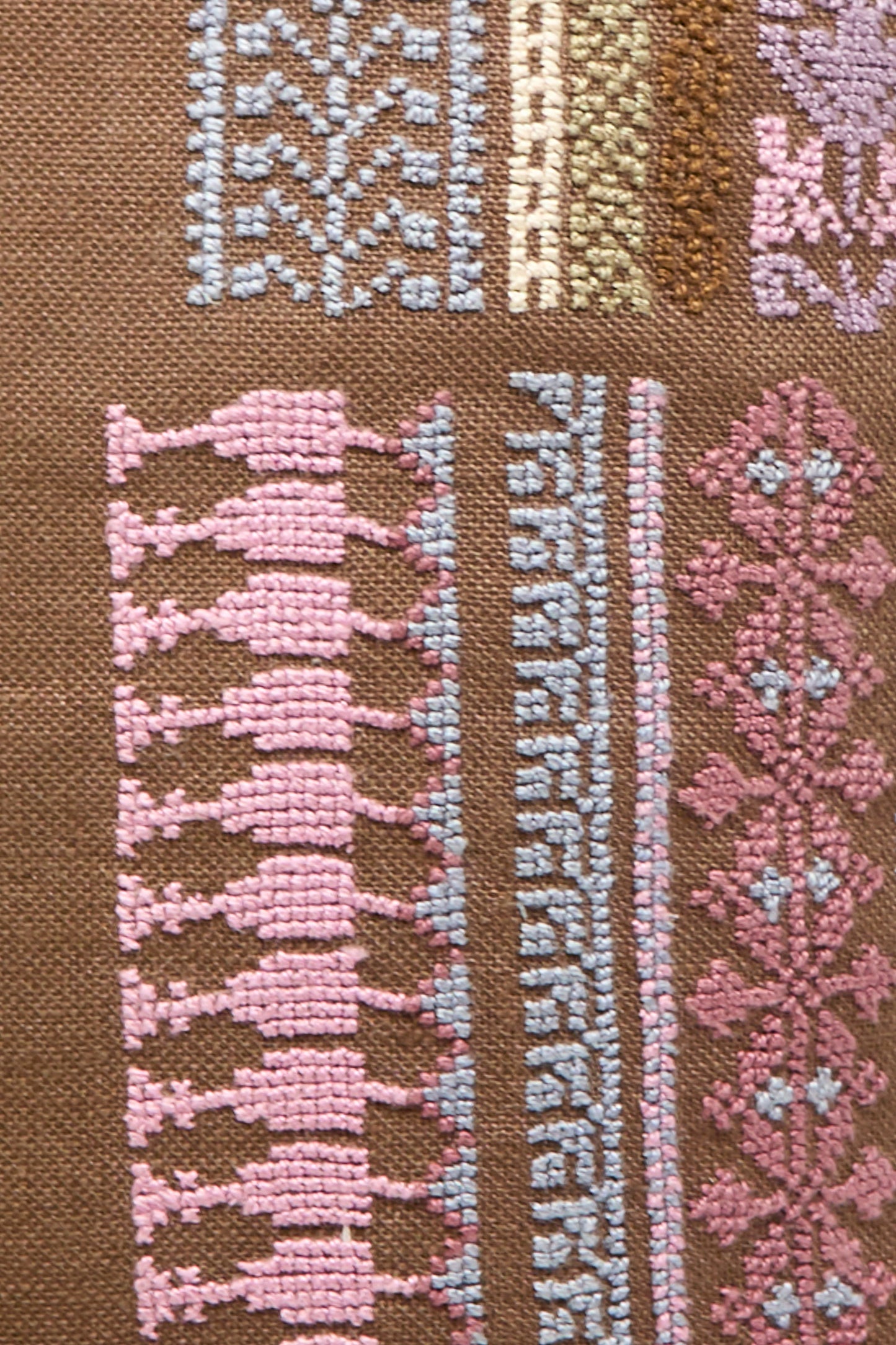 The Kissweh Imm Bushra Hand Embroidered Pillow in Chocolate showcases brown fabric with geometric and floral embroidery in pink, blue, and brown, arranged in striking patterns, and includes a plush down feather insert for comfort.