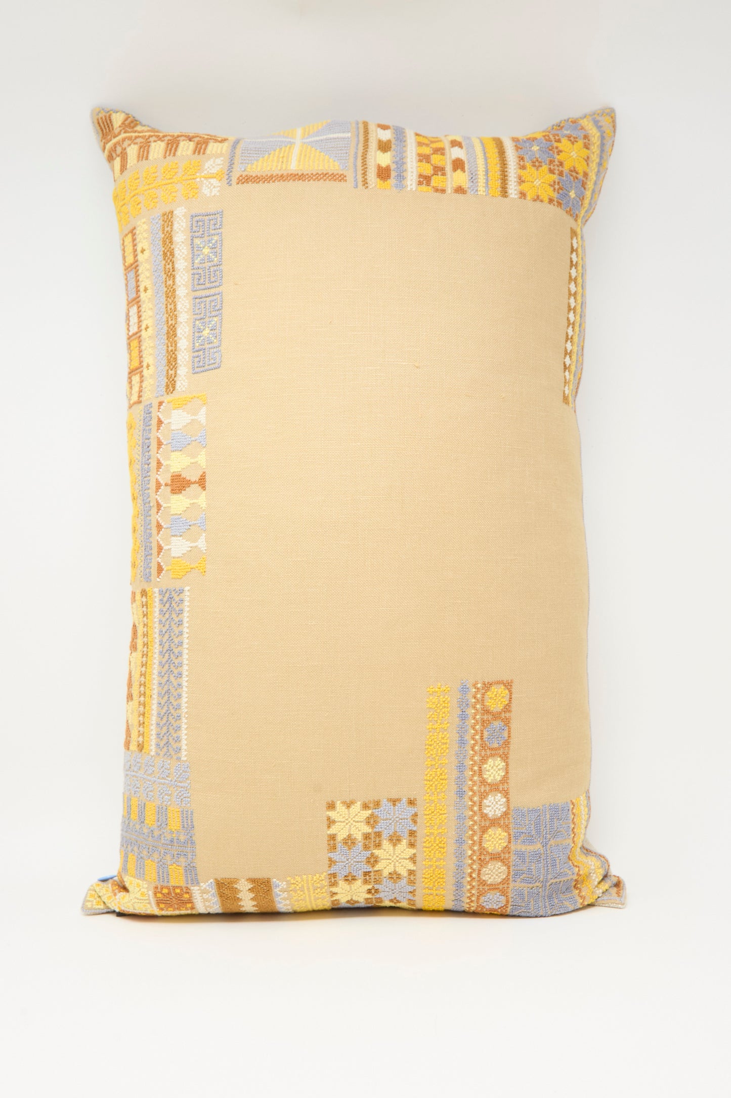 The Kissweh Imm Bushra Hand Embroidered Pillow in Mustard is a rectangular Belgian linen cushion, featuring hand-embroidered patchwork in yellow, gold, and light blue at the corners on a plain white background.